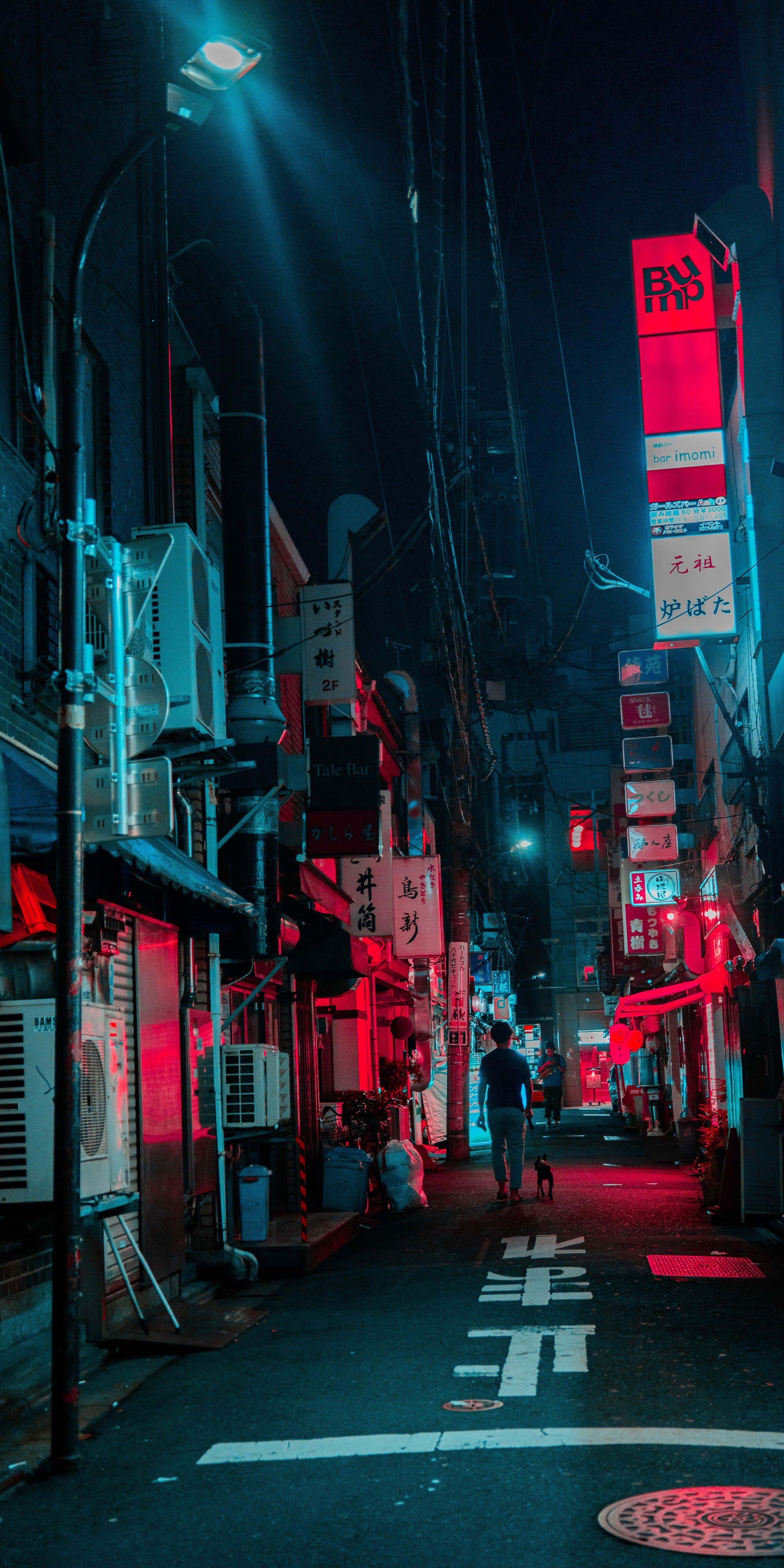 Dark Cyberpunk 桌布 壁紙 — 一個孤獨的身影在夜晚走下一條霓虹燈照亮的東京小巷，紅色和藍色的燈光在潮濕的路面上投下戲劇性的陰影。