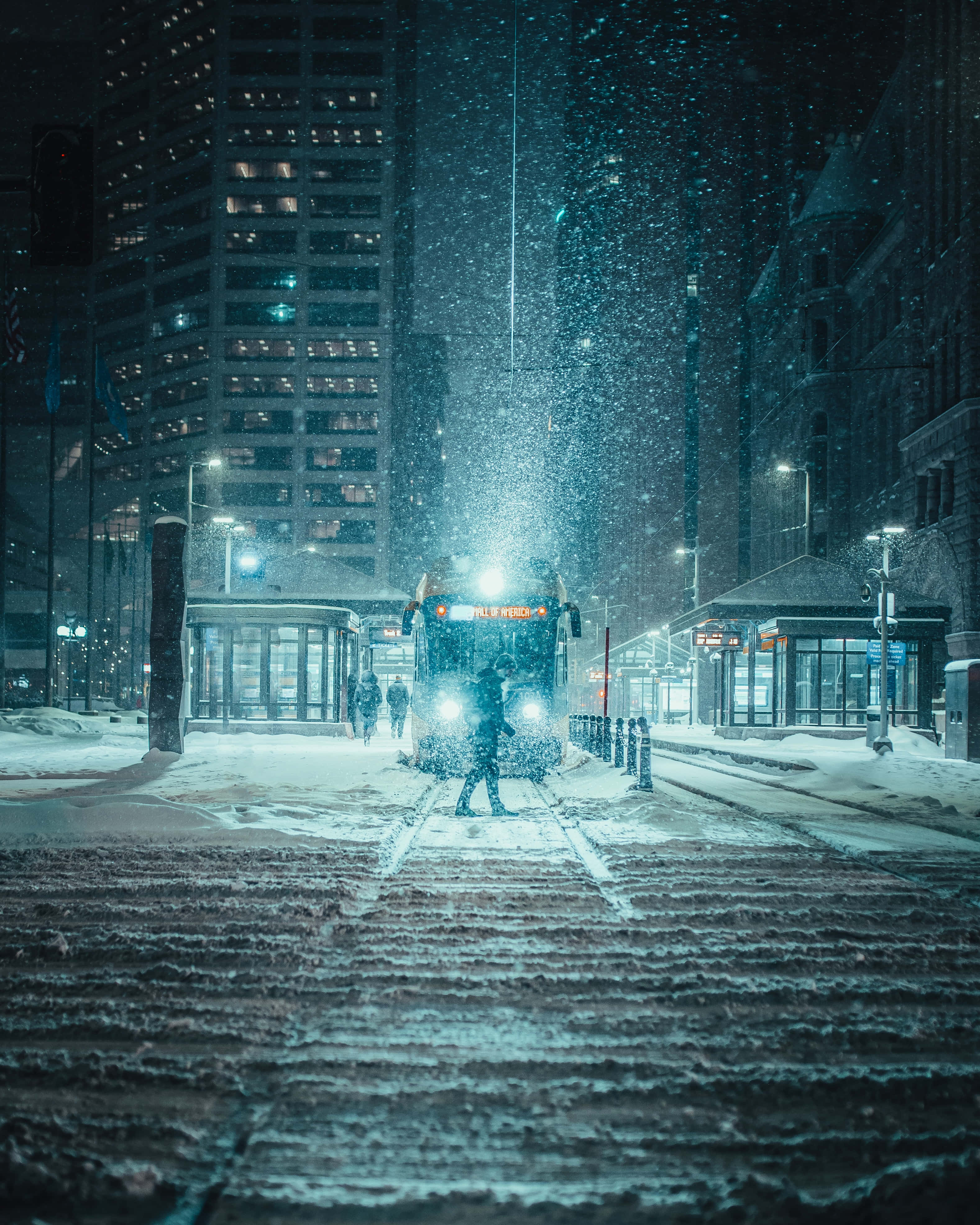 Simple Winter 桌布 壁紙 — 一個孤獨的身影在夜晚走向一輛被雪覆蓋的城市巴士，雪花在閃爍的路燈下飄落。