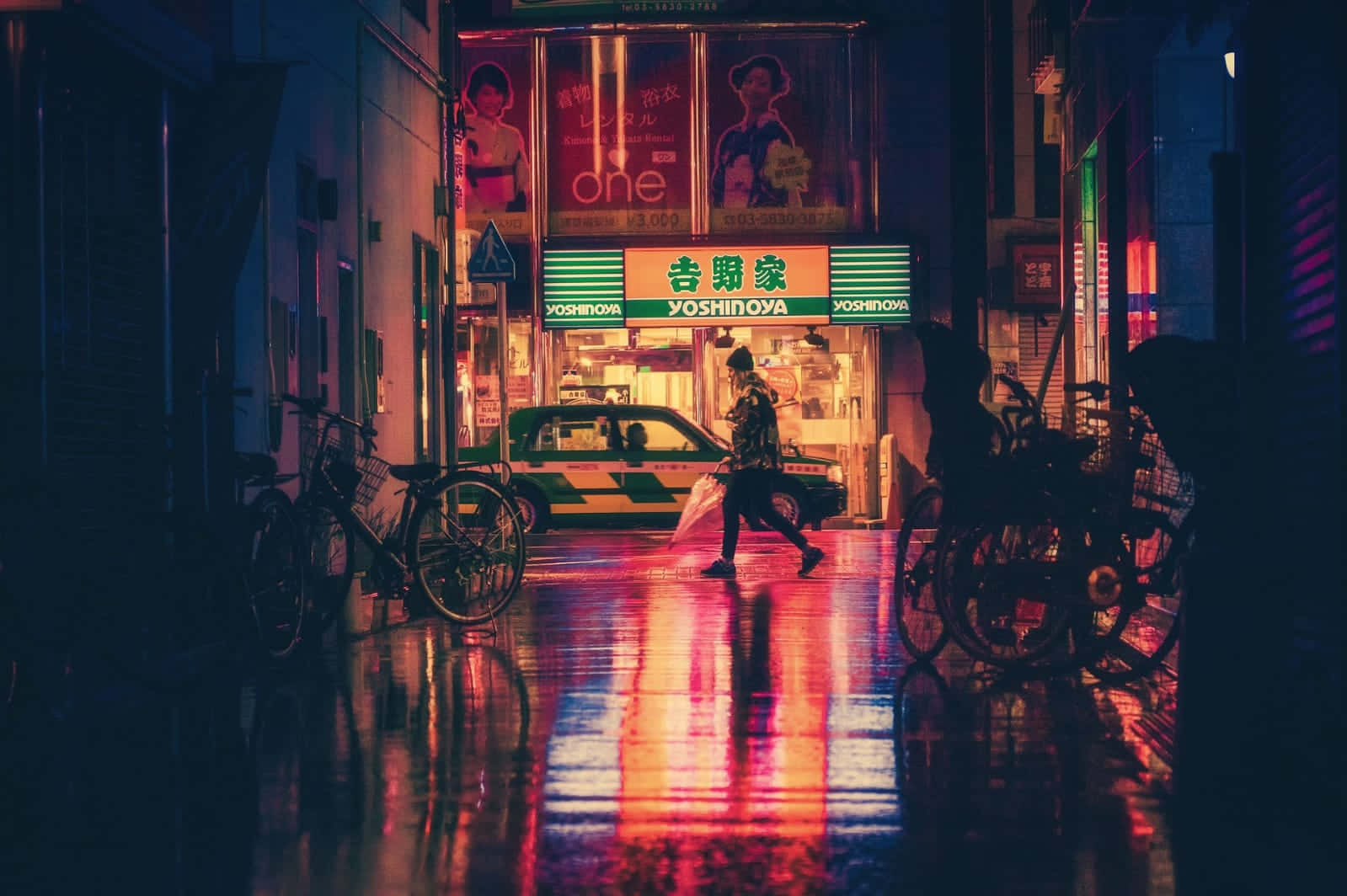 City Street 桌布 壁紙 — 一個孤獨的身影在夜晚走過東京一條被霓虹燈浸透的小巷，雨水濕滑的路面反射出鮮豔的紅色和綠色招牌。
