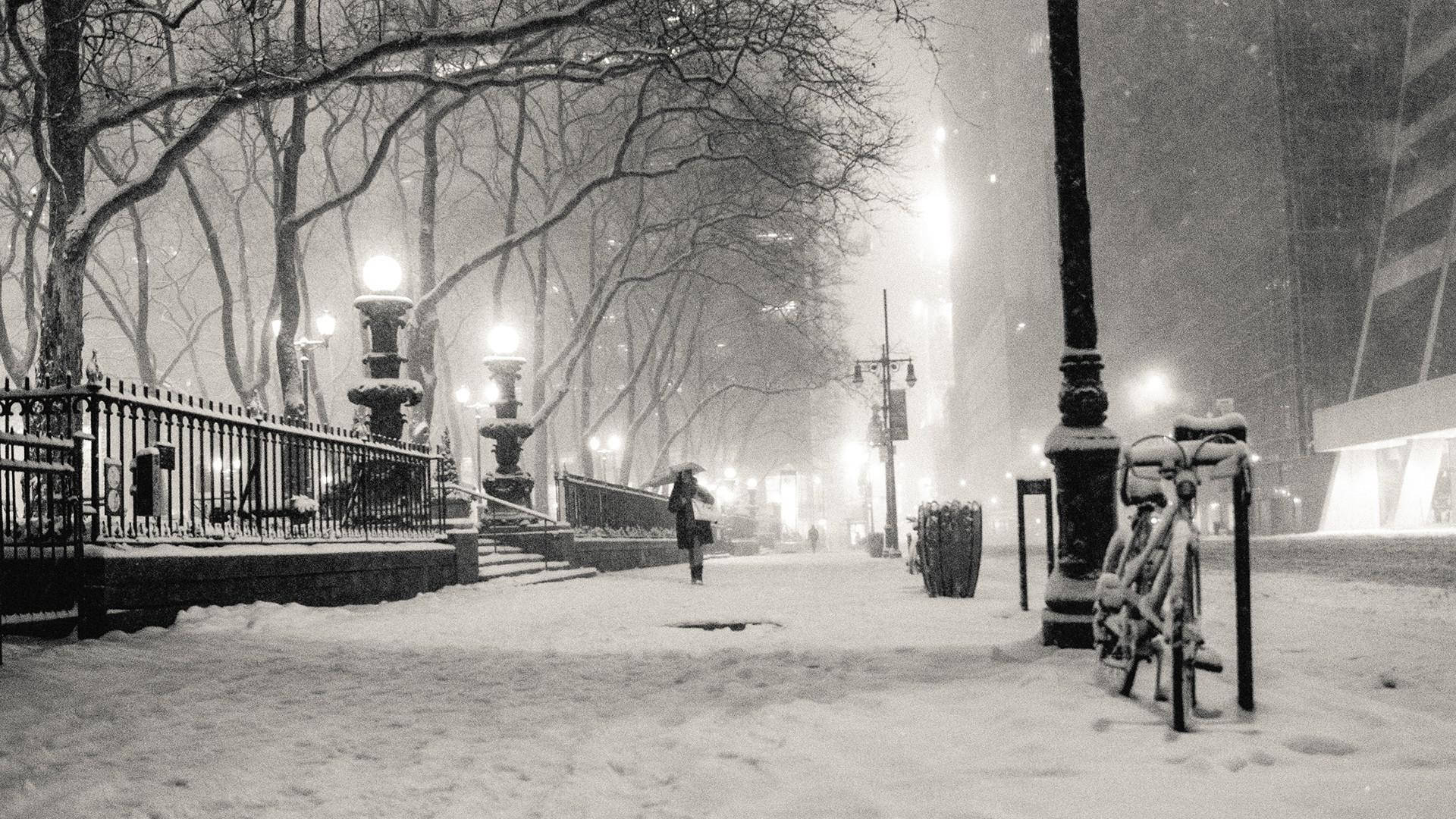 New York 桌布 壁紙 — 一個孤獨的身影在夜晚走過白雪覆蓋的城市公園，在發光的街燈下，附近有光禿禿的樹木和灑滿雪的腳踏車。