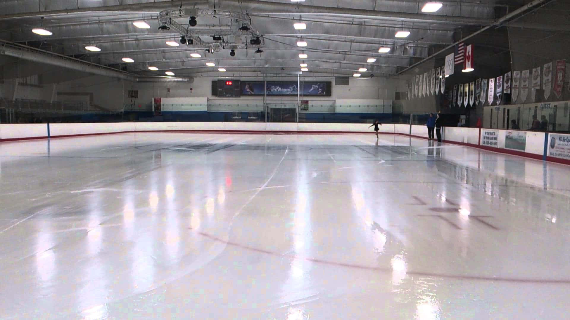 Ice Rink 桌布 壁紙 — 一個孤獨的身影在寬闊閃亮的室內溜冰場上滑行，上方有明亮的燈光，牆上掛滿橫幅。