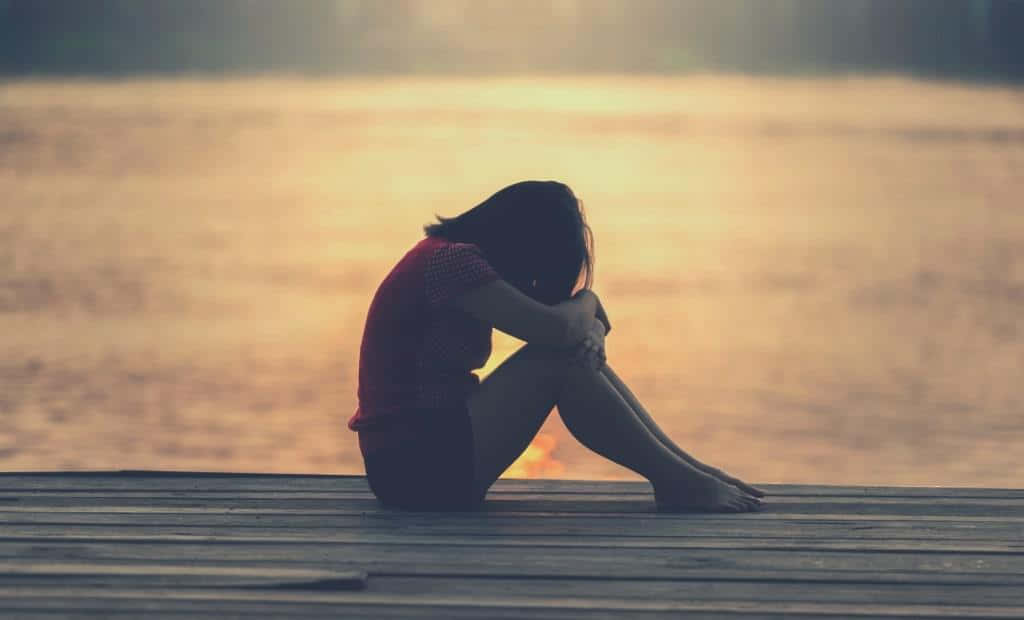 Lonely 桌布 壁紙 — 一個孤獨的身影在日落時分蜷縮在木製碼頭上，剪影映襯著閃爍的金色水面地平線。