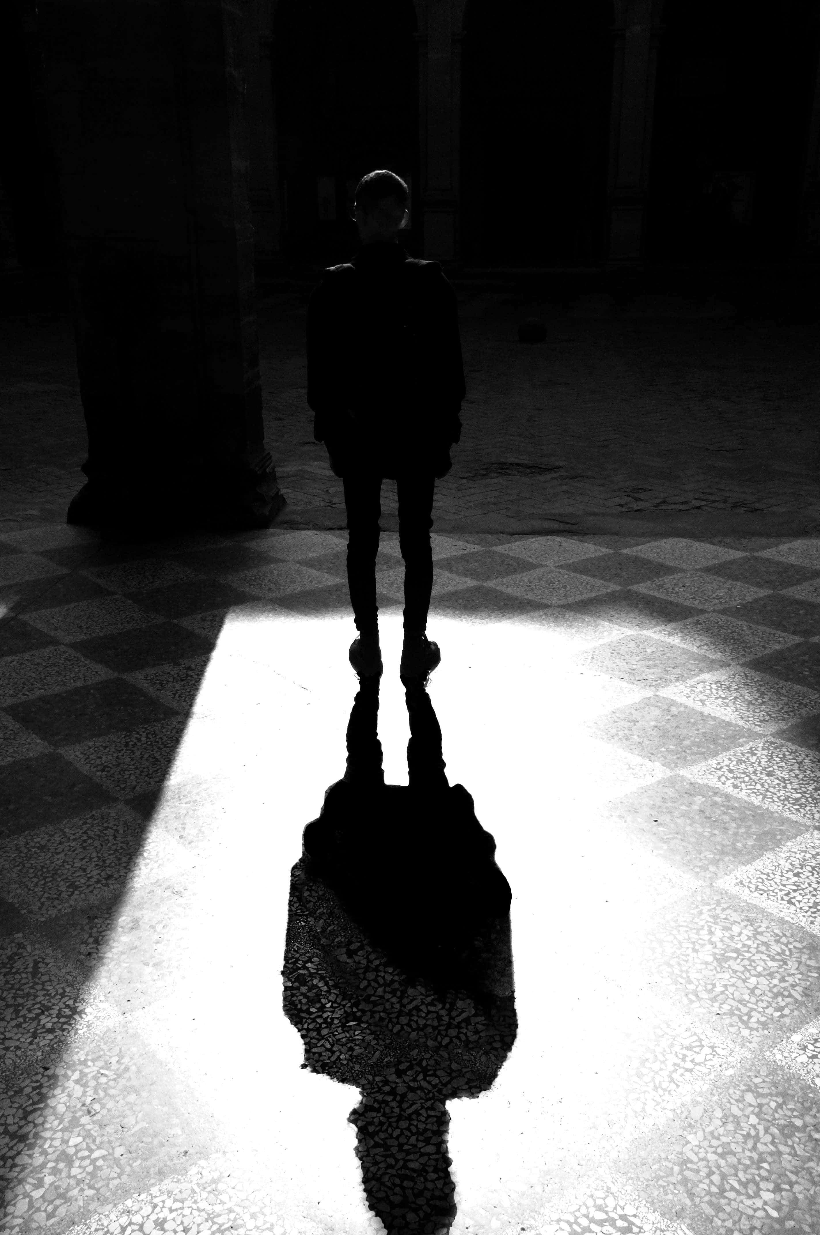 shadow 桌布 壁紙 — 一個孤獨的身影在昏暗的大廳中呈現鮮明的剪影，他們拉長的影子在棋盤格地板上的戲劇性光束中延伸。