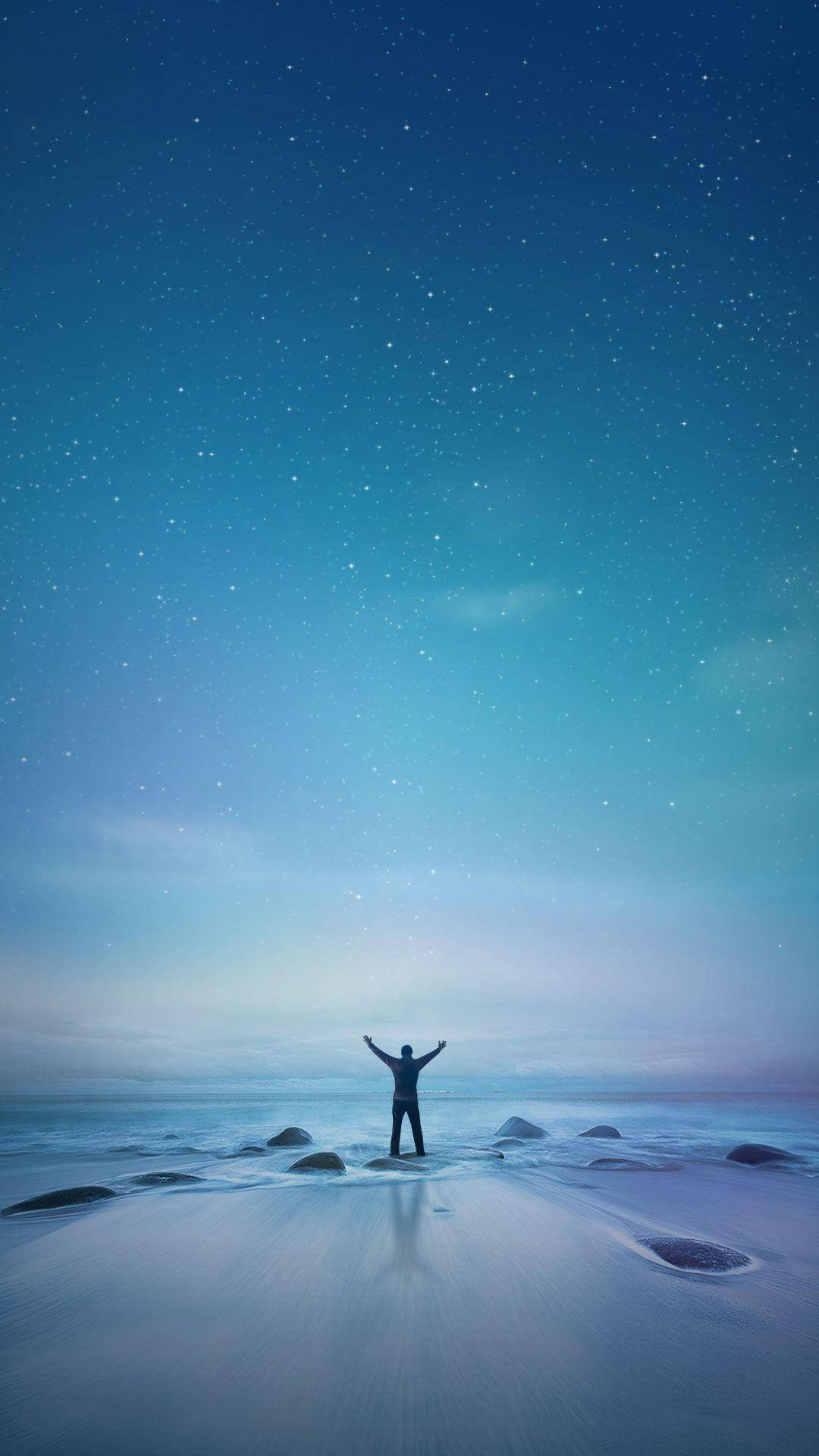 Xiaomi 桌布 壁紙 — 一個孤獨的身影在星光閃爍的海灘上舉起雙臂，站在廣闊的漸變天空下。