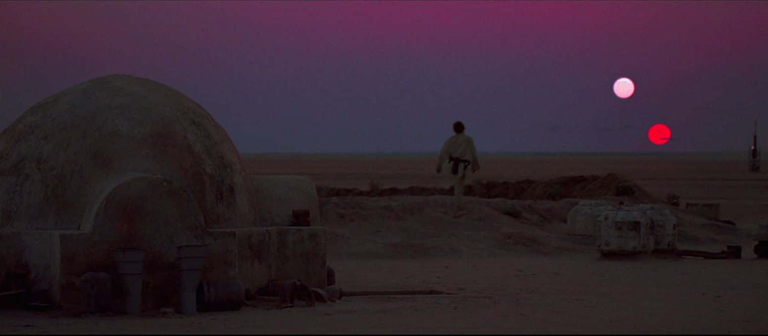 A New Hope 桌布 壁紙 — 一個孤獨的身影在暮色中穿越沙漠景觀，天空中有兩個發光的太陽，一個粉紅色，一個紅色。