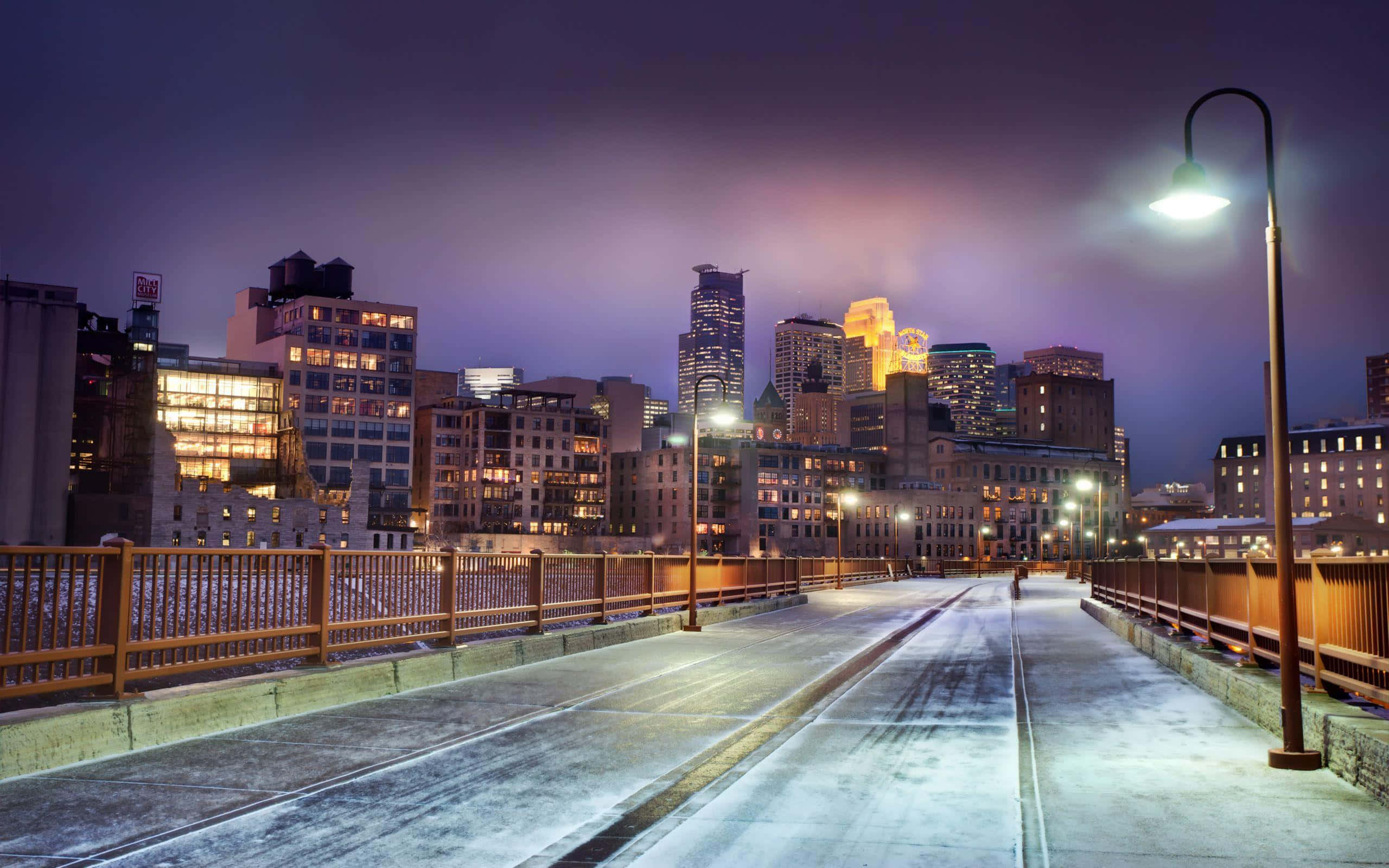 Winter Cityscape 桌布 壁紙 — 一個孤獨的身影在暮色中走過寧靜的城市橋樑，燈火通明的摩天大樓在紫色天空下閃耀。