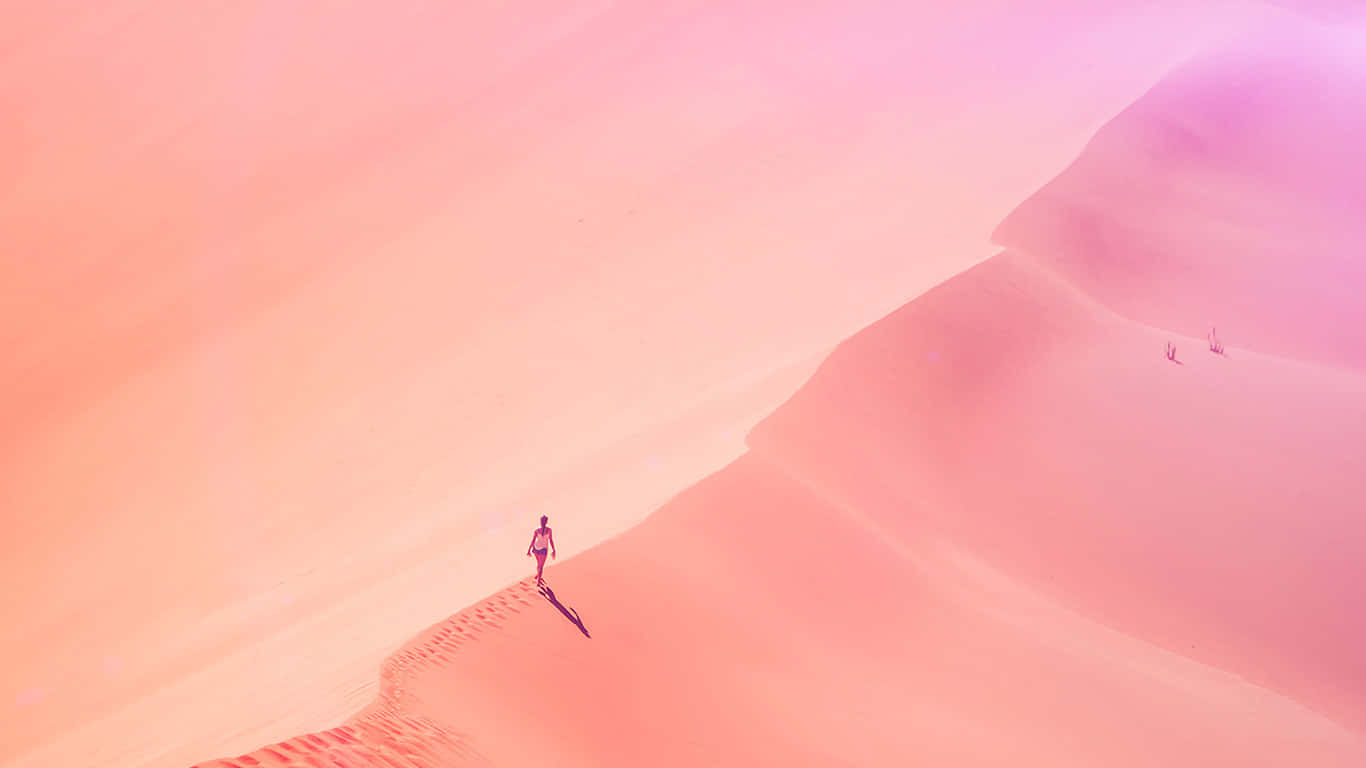 Pastel Minimalist 桌布 壁紙 — 一個孤獨的身影在柔和發光的天空下走過廣闊的粉紅色沙丘。