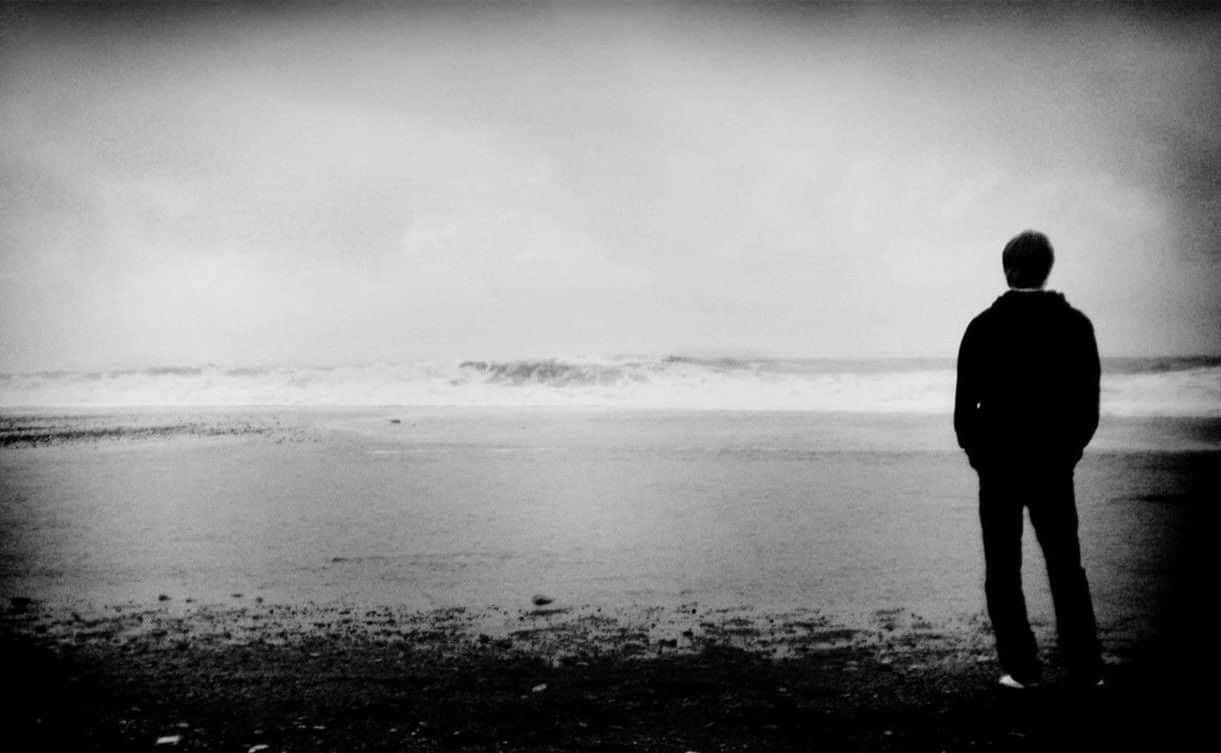 海灘 桌布 壁紙 — 一個孤獨的身影在濕漉漉的海灘上以剪影站立，面對著陰天天空下翻騰的海浪。