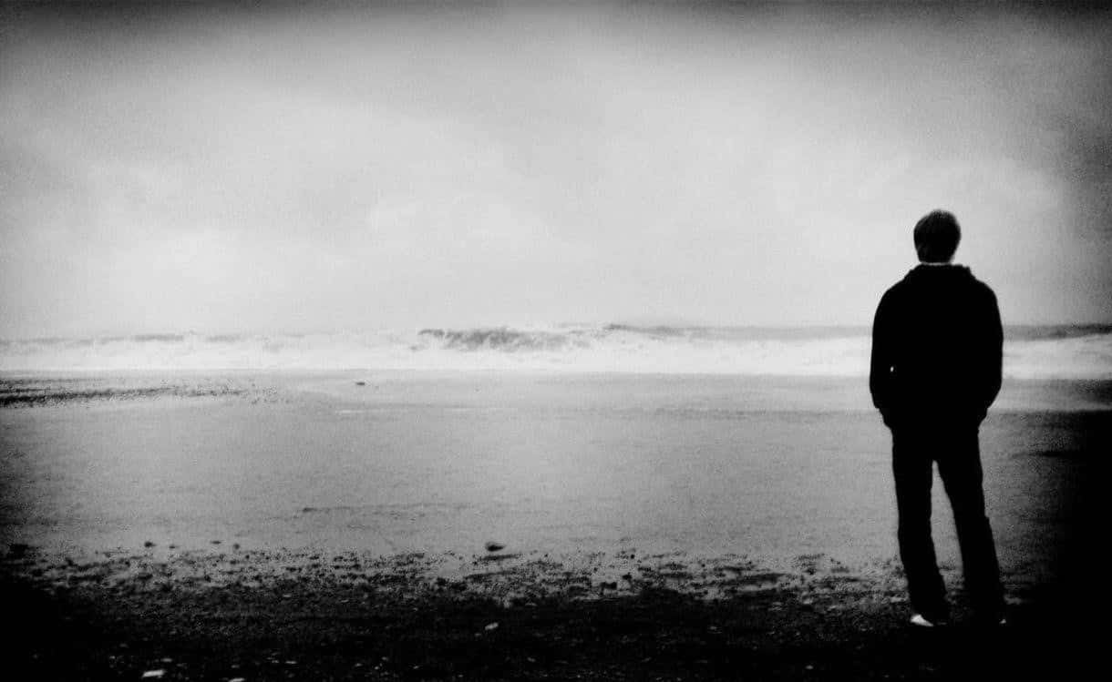 Silhouette 桌布 壁紙 — 一個孤獨的身影在濕漉漉的海灘上以剪影站立，面對著陰天天空下翻騰的海浪。