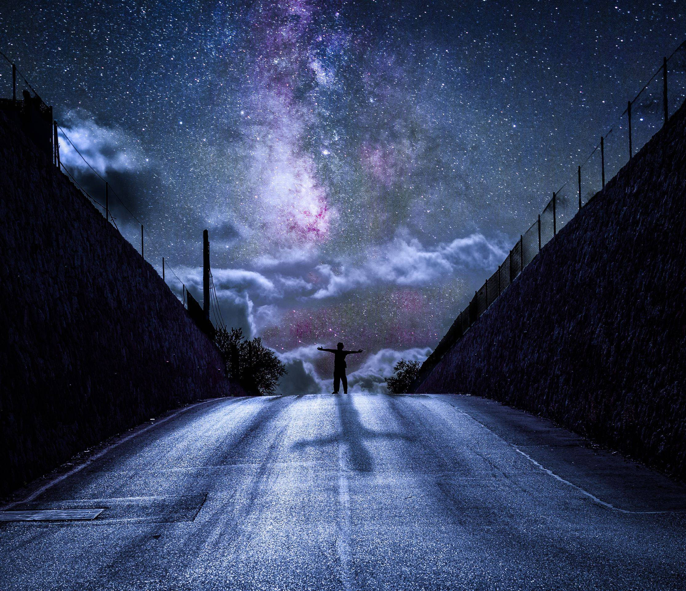 銀河 桌布 壁紙 — 一個孤獨的身影在狹窄的道路上張開雙臂，站在充滿銀河的壯麗星空下。