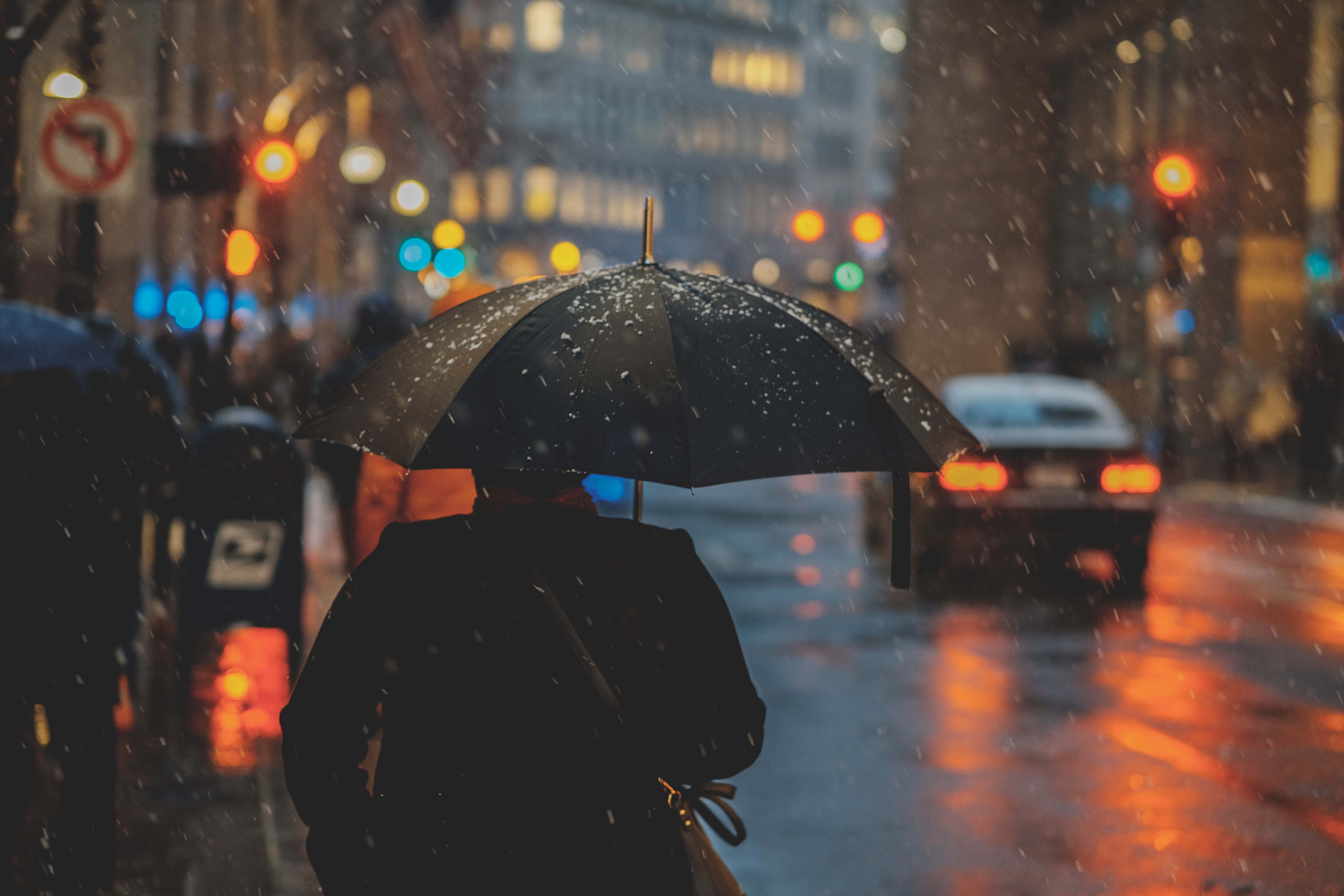 Man 桌布 壁紙 — 一個孤獨的身影在雨夜的街道上行走，手持黑色雨傘，濕漉漉的人行道反射著溫暖的街燈。