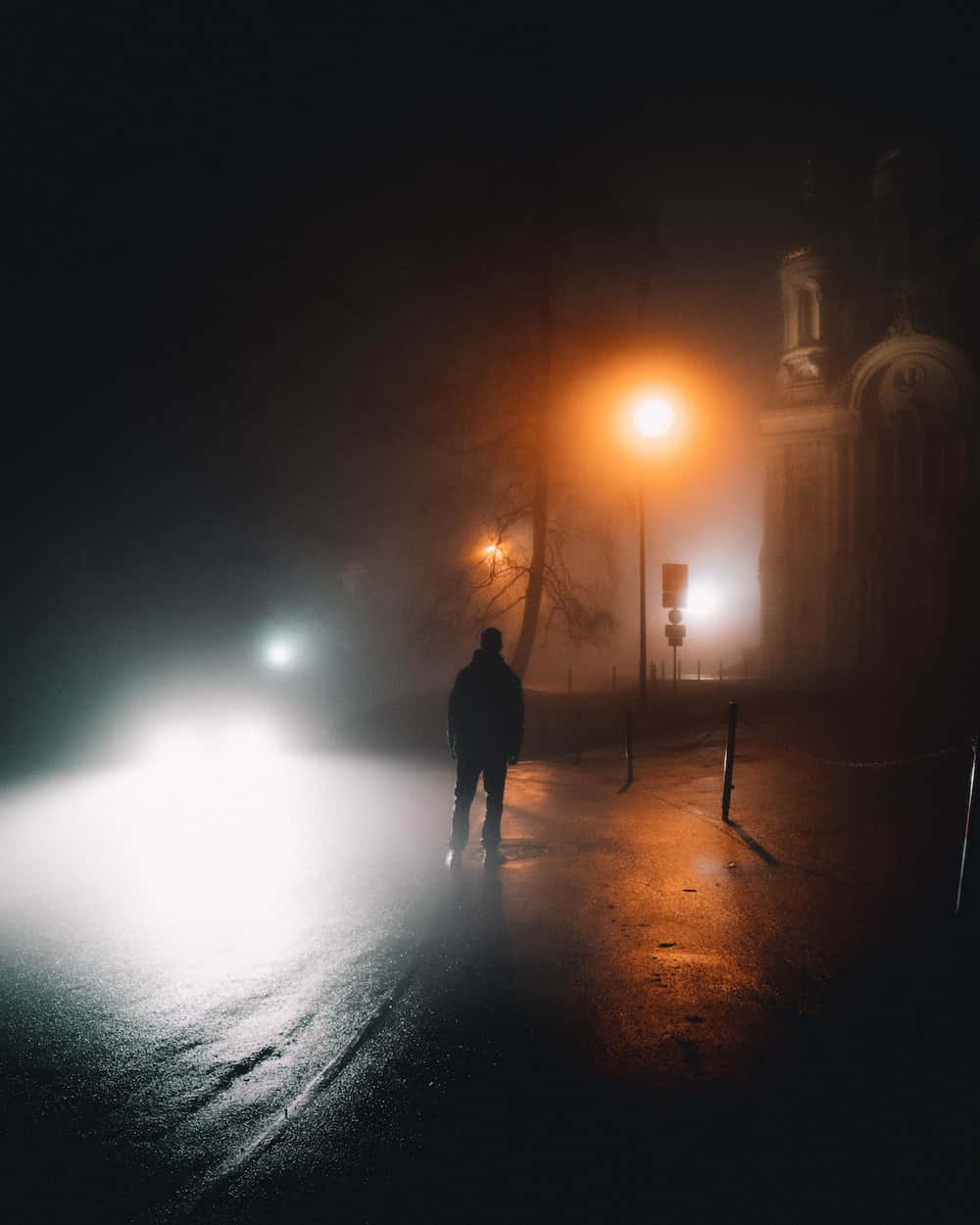 夜晚 桌布 壁紙 — 一個孤獨的身影在霧氣瀰漫的夜晚街道上行走，被溫暖的路燈和汽車明亮的車頭燈照亮。