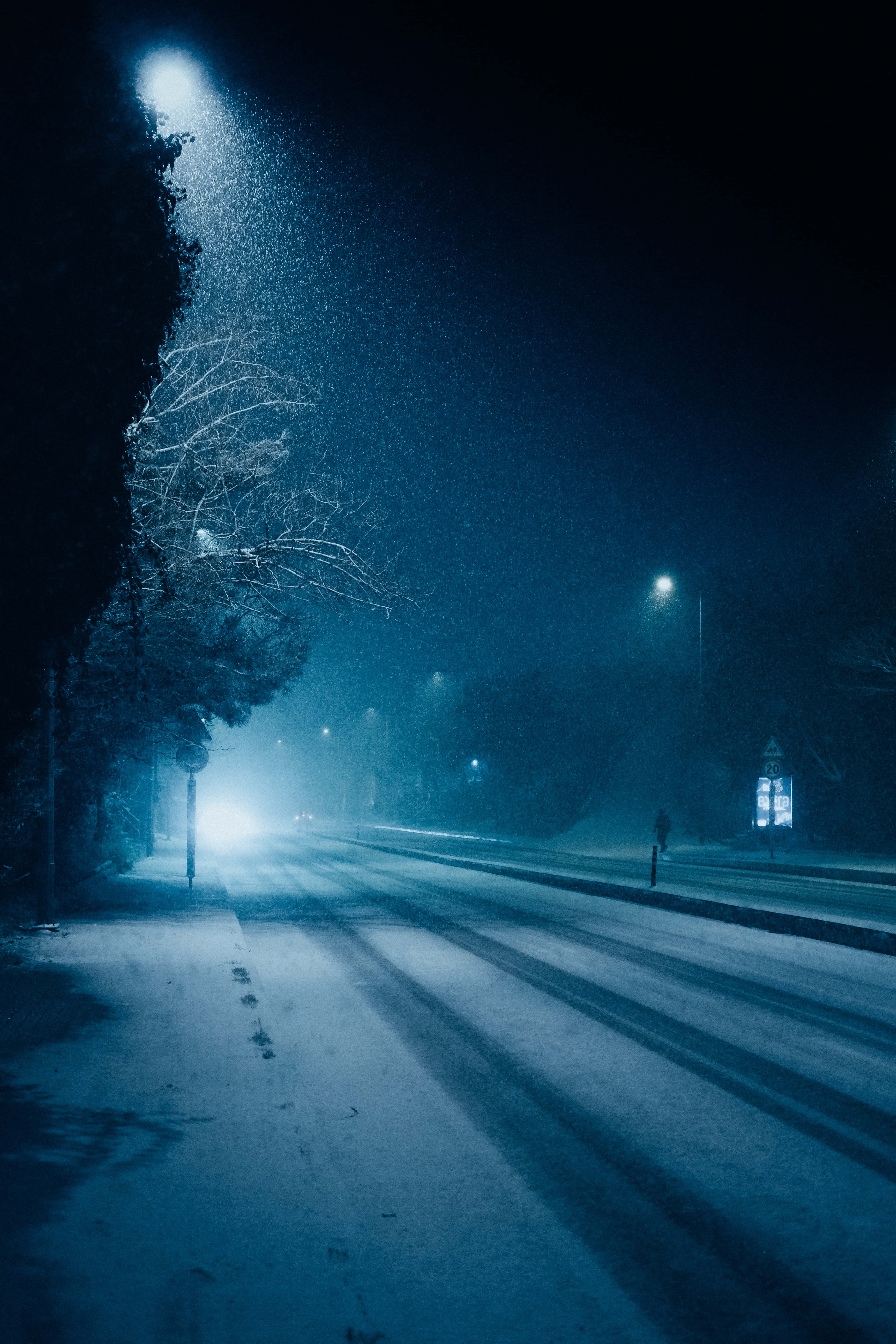 雪景 桌布 壁紙 — 一個孤獨的身影在霧濛濛的冬夜街道上行走，被冰冷的藍色路燈照亮，投下長長的影子。