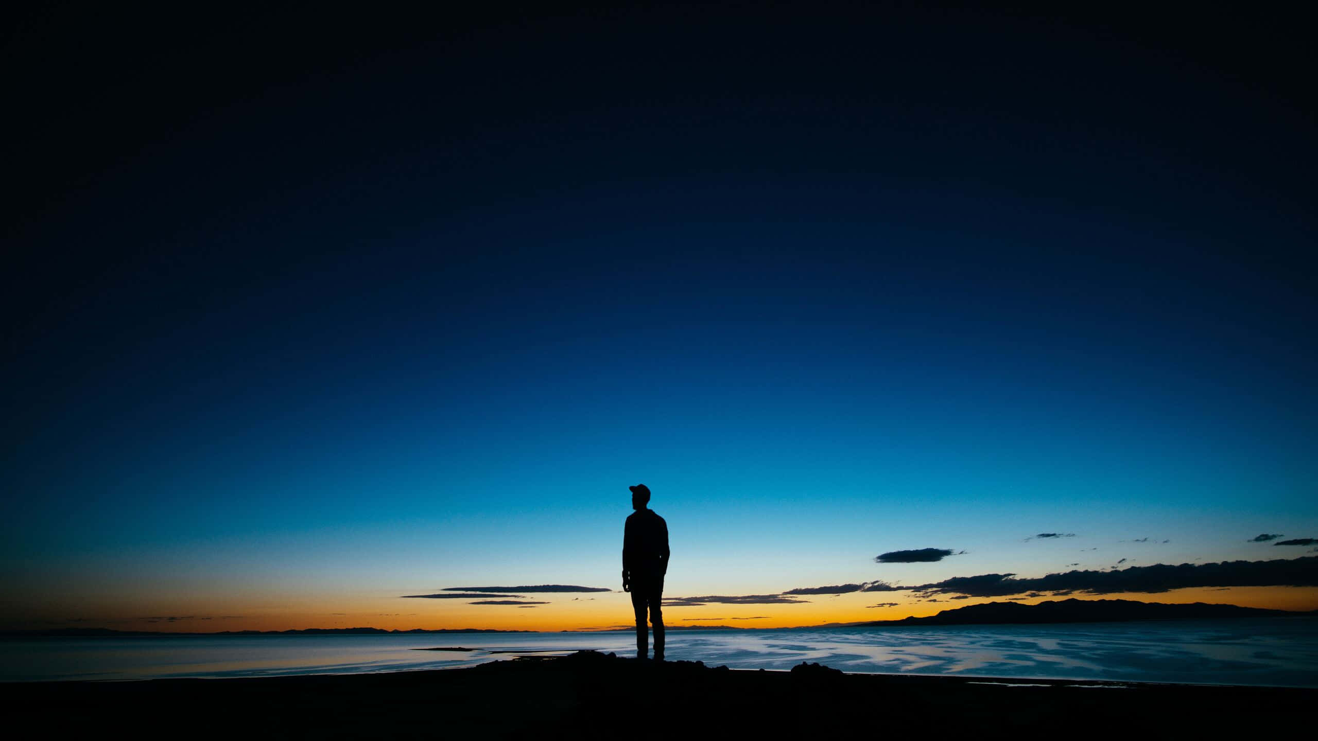 Alone 桌布 壁紙 — 一個孤獨的身影在黃昏時分站在懸崖上，眺望深藍與橙色漸變天空下的霧海。