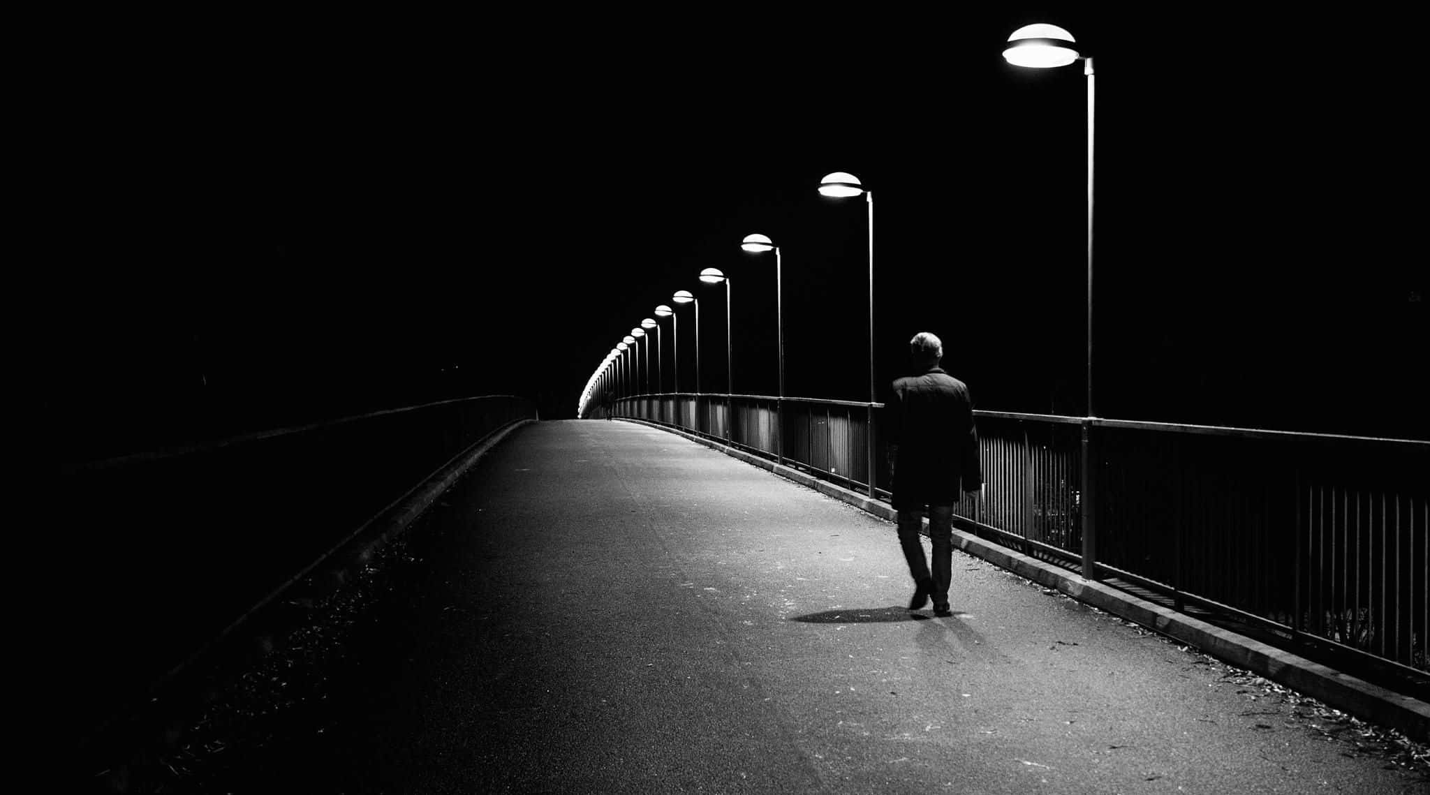 Alone 桌布 壁紙 — 一個孤獨的身影在黑夜中獨自沿著一條長長的照明橋樑行走，天空漆黑。