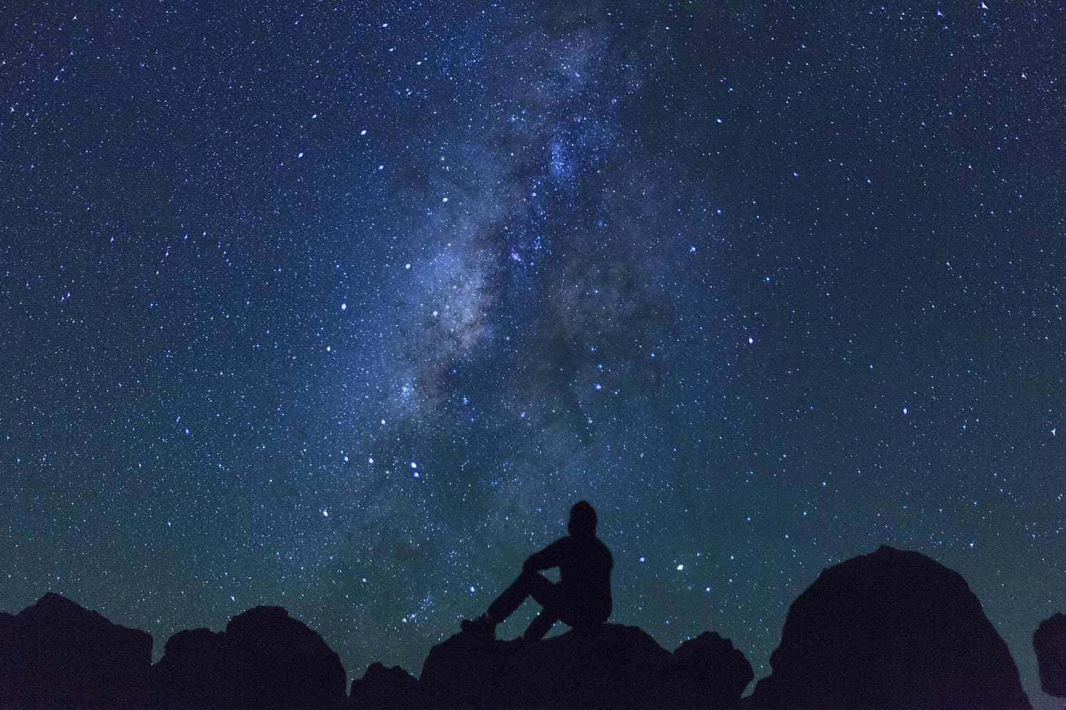Stars 桌布 壁紙 — 一個孤獨的身影坐在岩石地形上，仰望充滿銀河閃耀帶的壯麗星空。