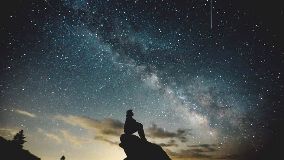 Stars 桌布 壁紙 — 一個孤獨的身影坐在岩石露頭上，仰望充滿銀河和流星的壯麗星空。