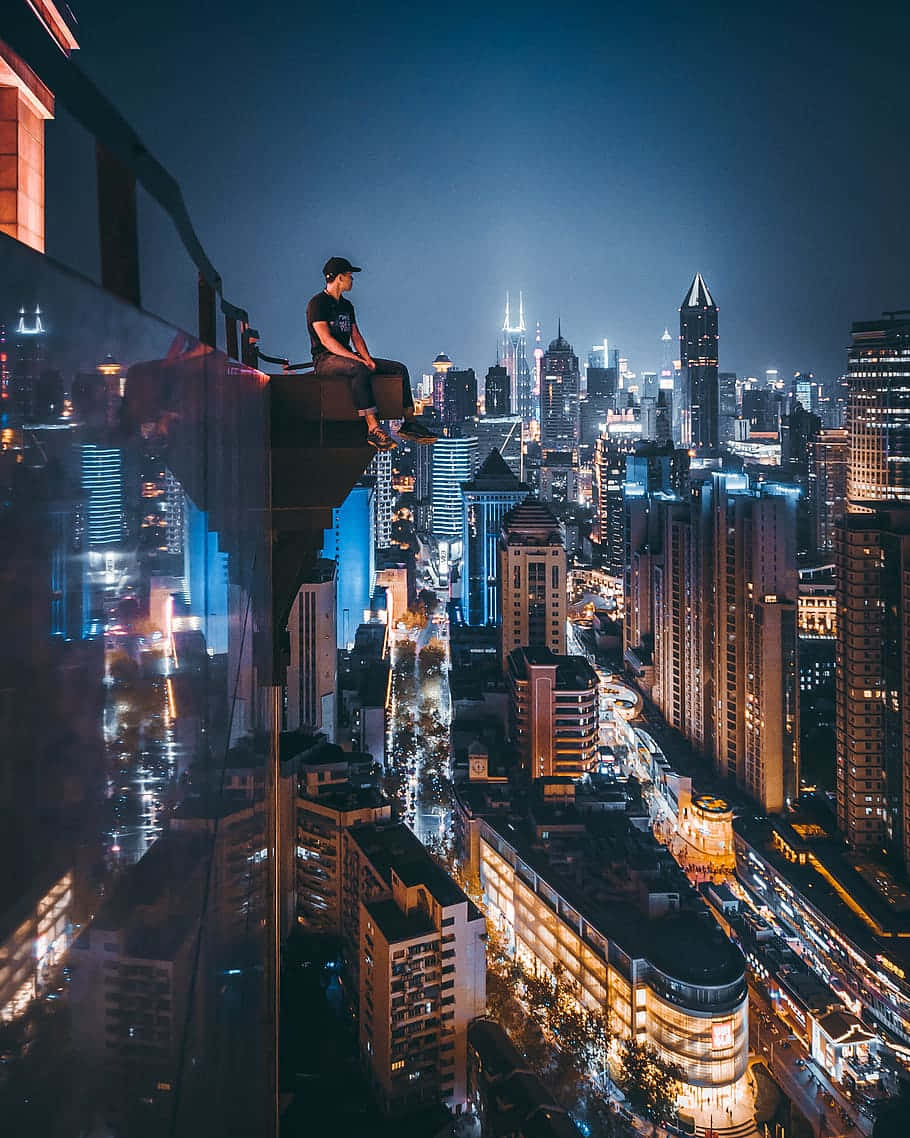 Rooftop 桌布 壁紙 — 一個孤獨的身影坐在摩天大樓的邊緣，俯瞰夜晚充滿活力的霓虹燈城市景觀，街道閃爍，建築高聳。