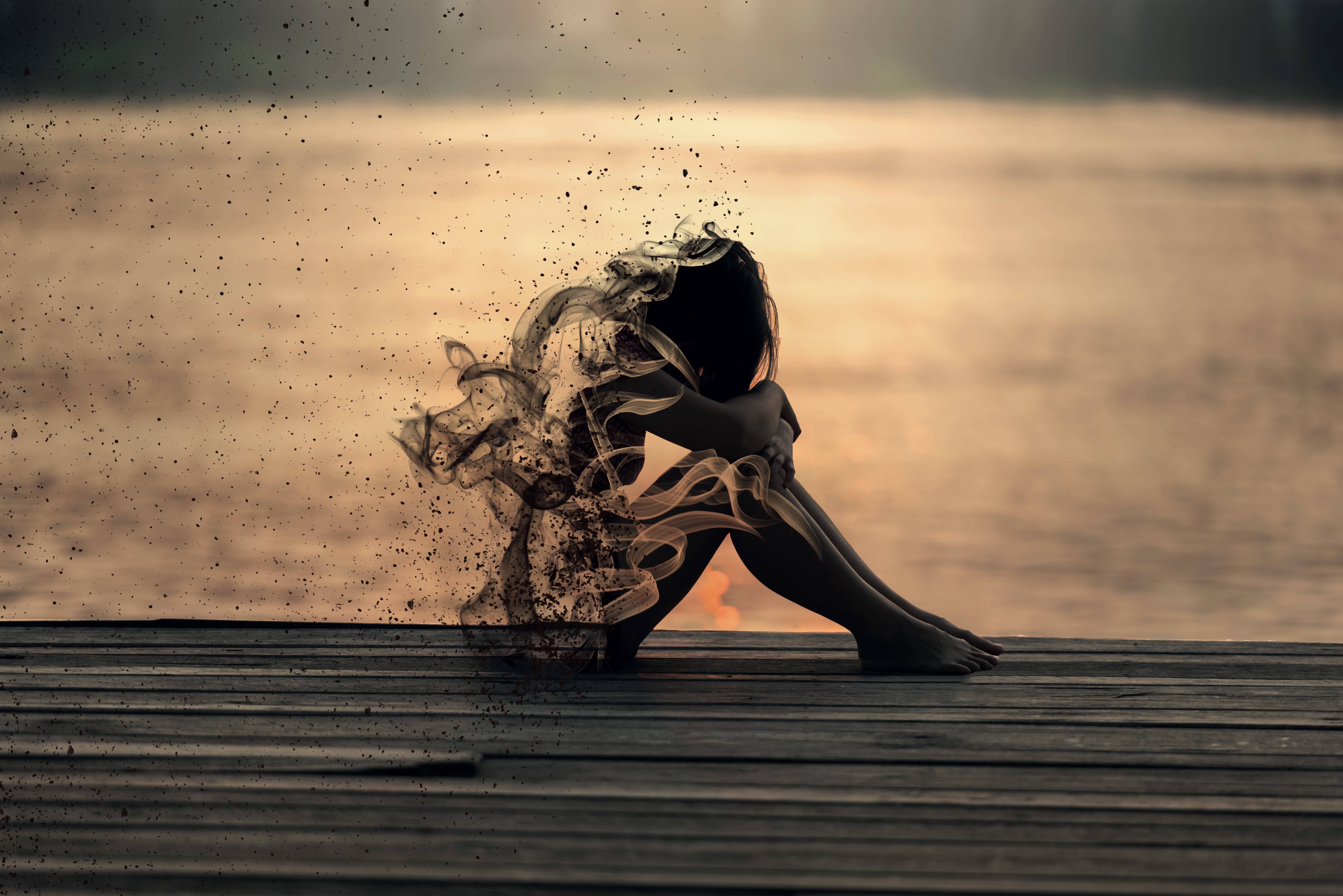 melancholy 桌布 壁紙 — 一個孤獨的身影坐在日落時分的木碼頭上，他們的身形在平靜的水面背景下化作旋轉的煙霧消散。