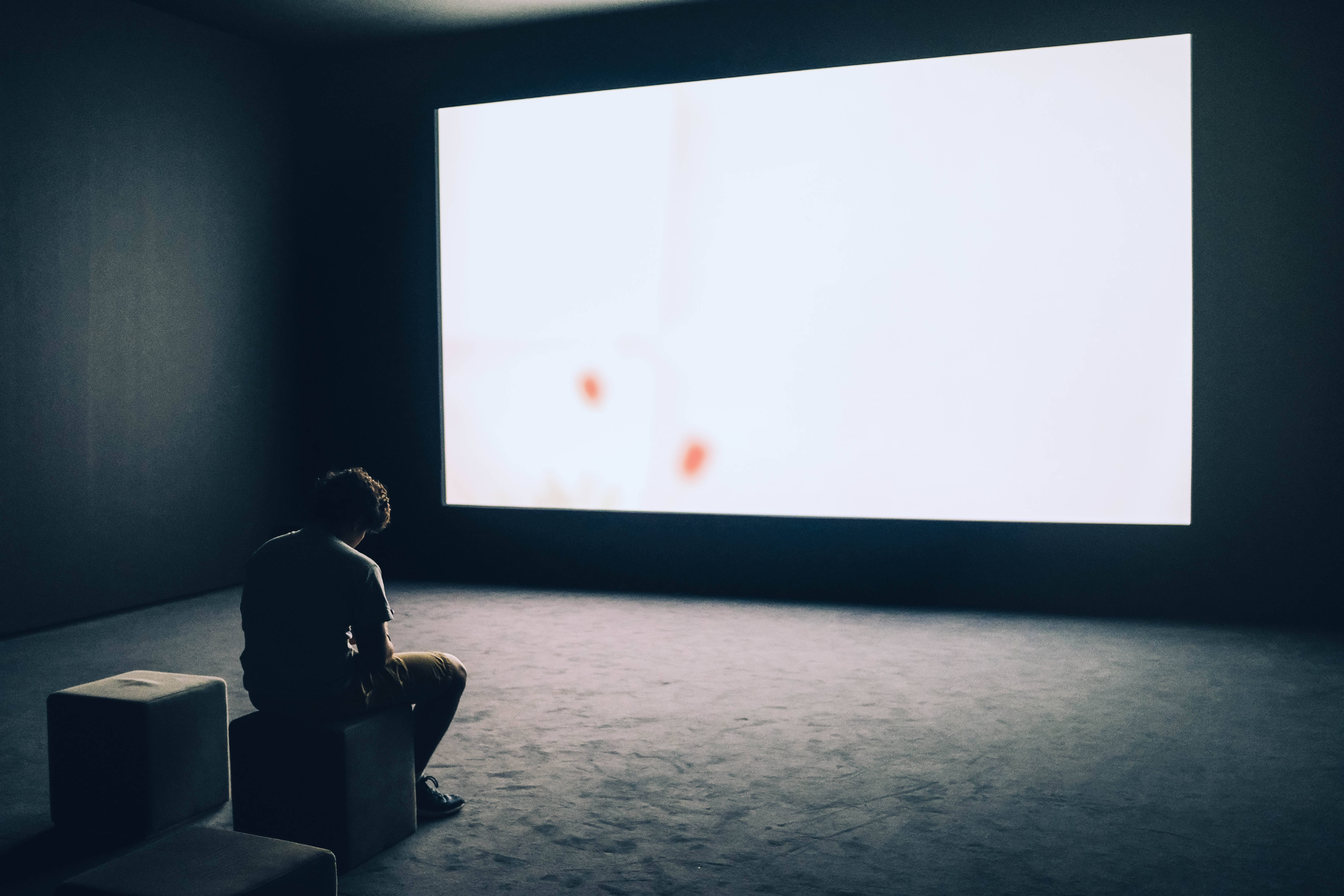 Alone Boy 桌布 壁紙 — 一個孤獨的身影坐在昏暗的房間裡，看著大螢幕上明亮的抽象投影。