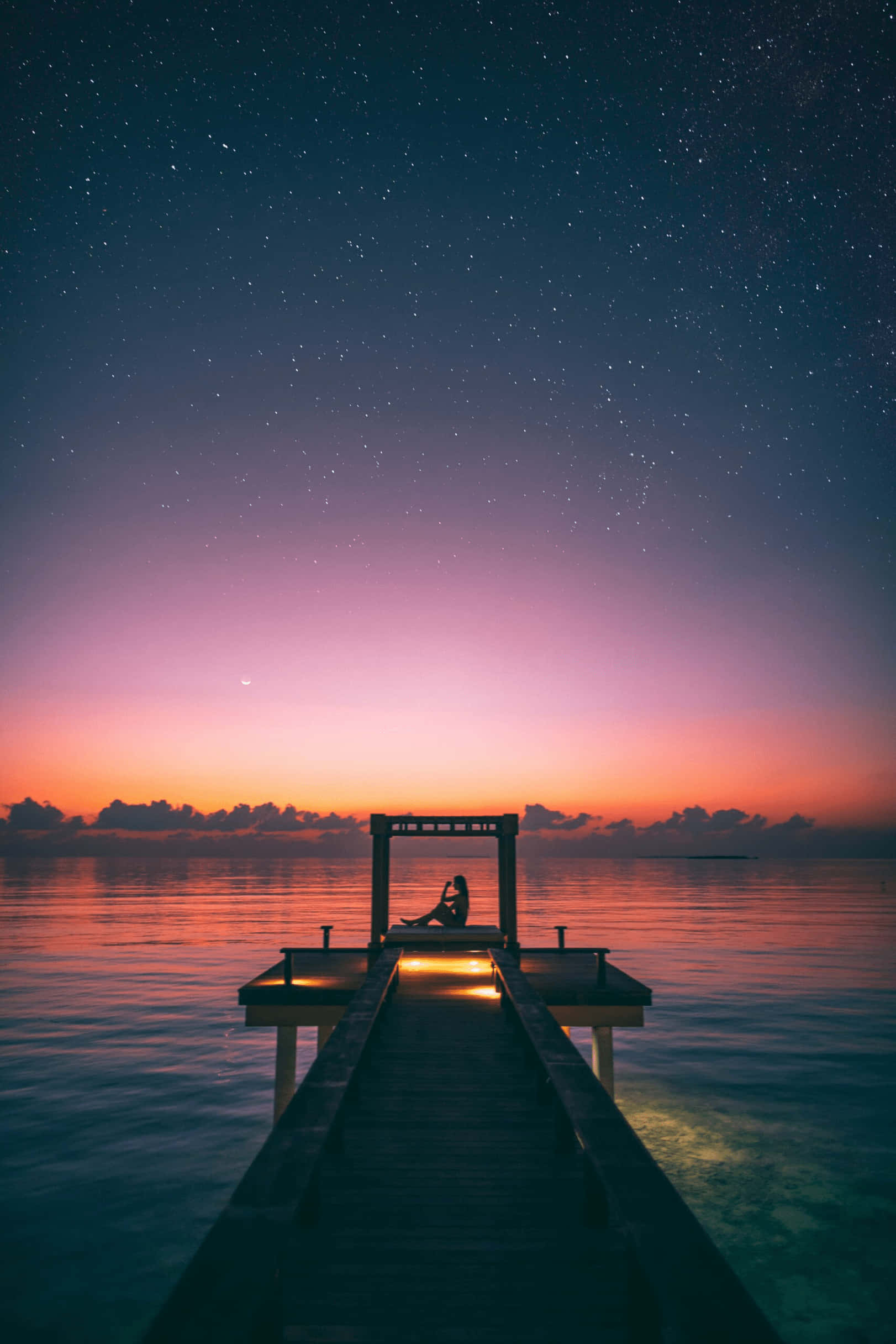Starry 桌布 壁紙 — 一個孤獨的身影坐在木製碼頭上，星空暮色天空帶有粉紅、橙色和深藍色漸變，倒映在平靜的水面上。