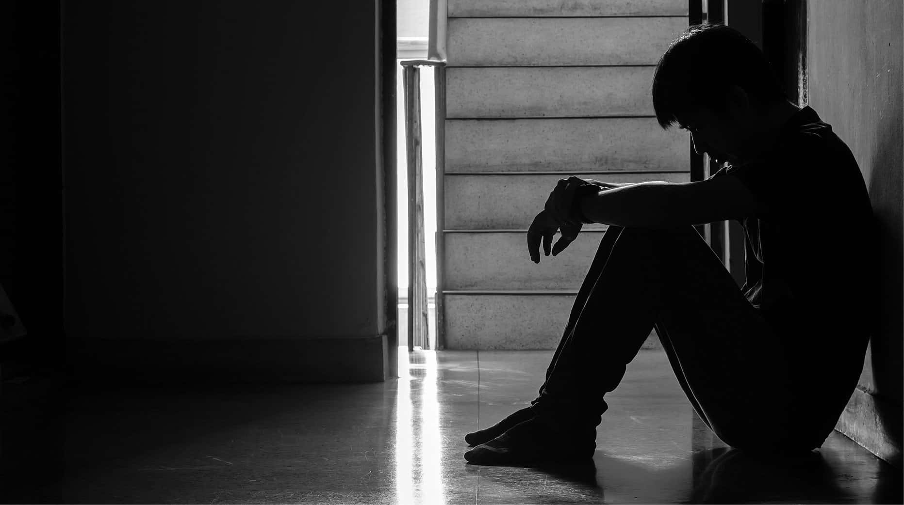 Depressed 桌布 壁紙 — 一個孤獨的身影坐在樓梯底部的陰影寂靜中，沐浴在強烈的背光下。