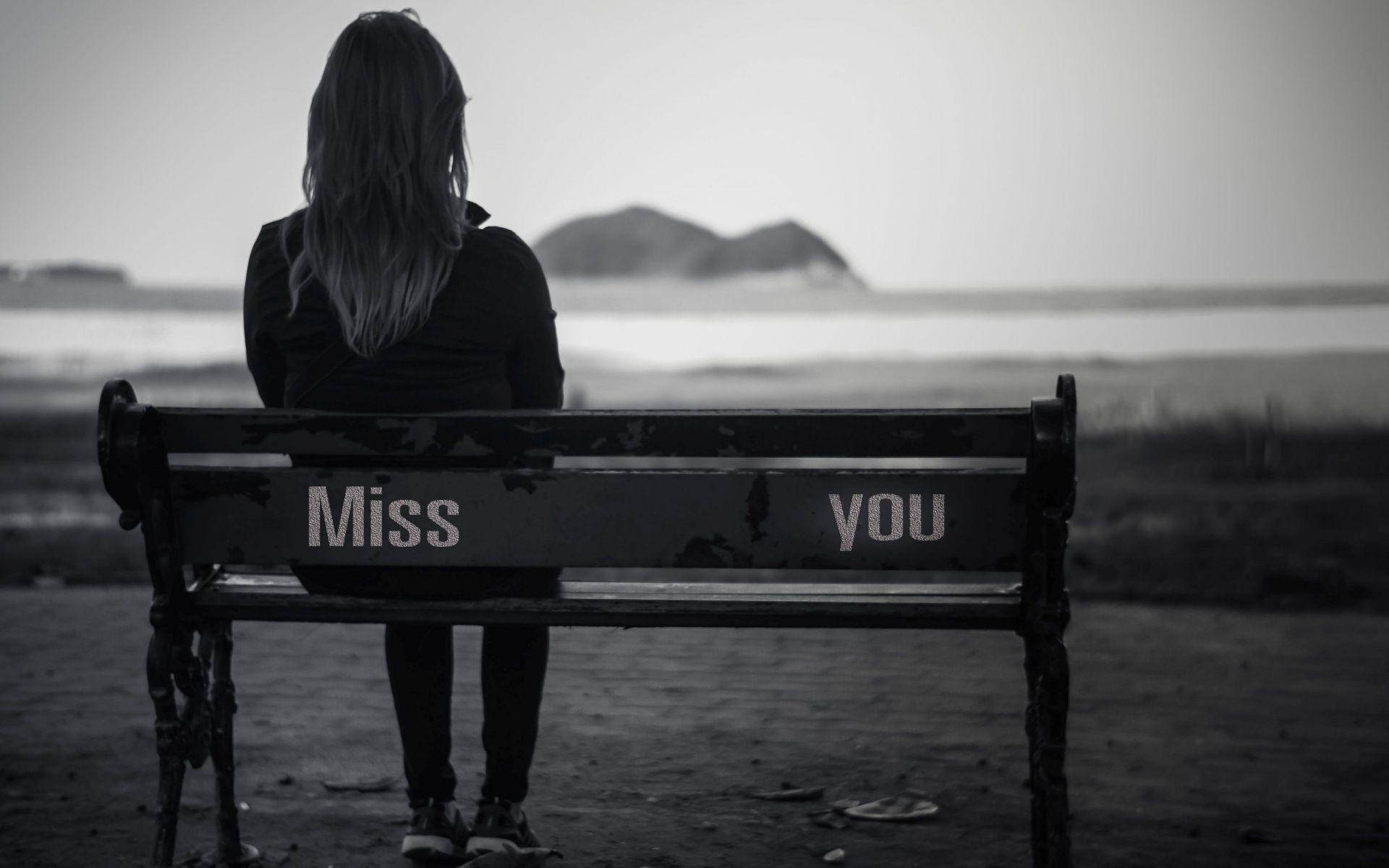 miss you 桌布 壁紙 — 一個孤獨的身影坐在水邊一張經風化的長椅上，椅背以灰階繪有「Miss you」字樣。