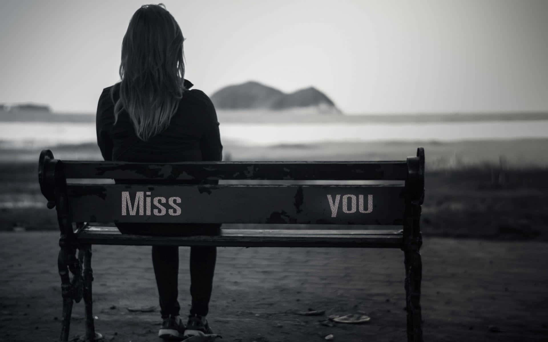 heartbreak 桌布 壁紙 — 一個孤獨的身影坐在水邊一張飽經風霜的長椅上，椅背上以單色調繪有「Miss you」字樣。