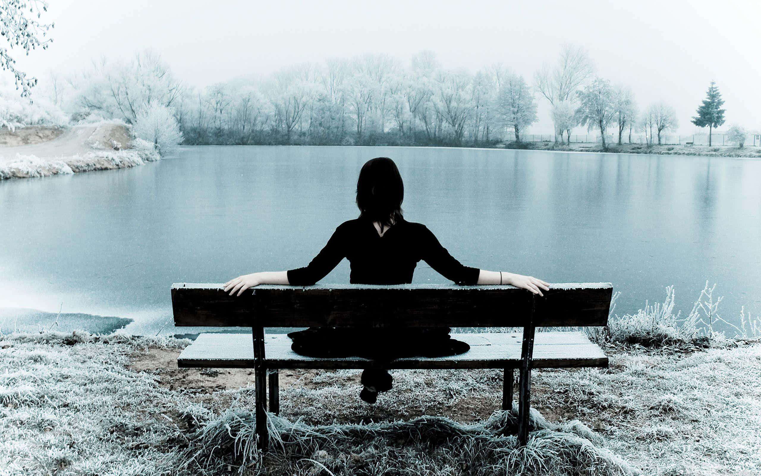 Lonely Girl 桌布 壁紙 — 一個孤獨的身影坐在結霜的長椅上，俯瞰著被霧氣籠罩的冰凍湖泊，周圍是光禿禿的冬季樹木。