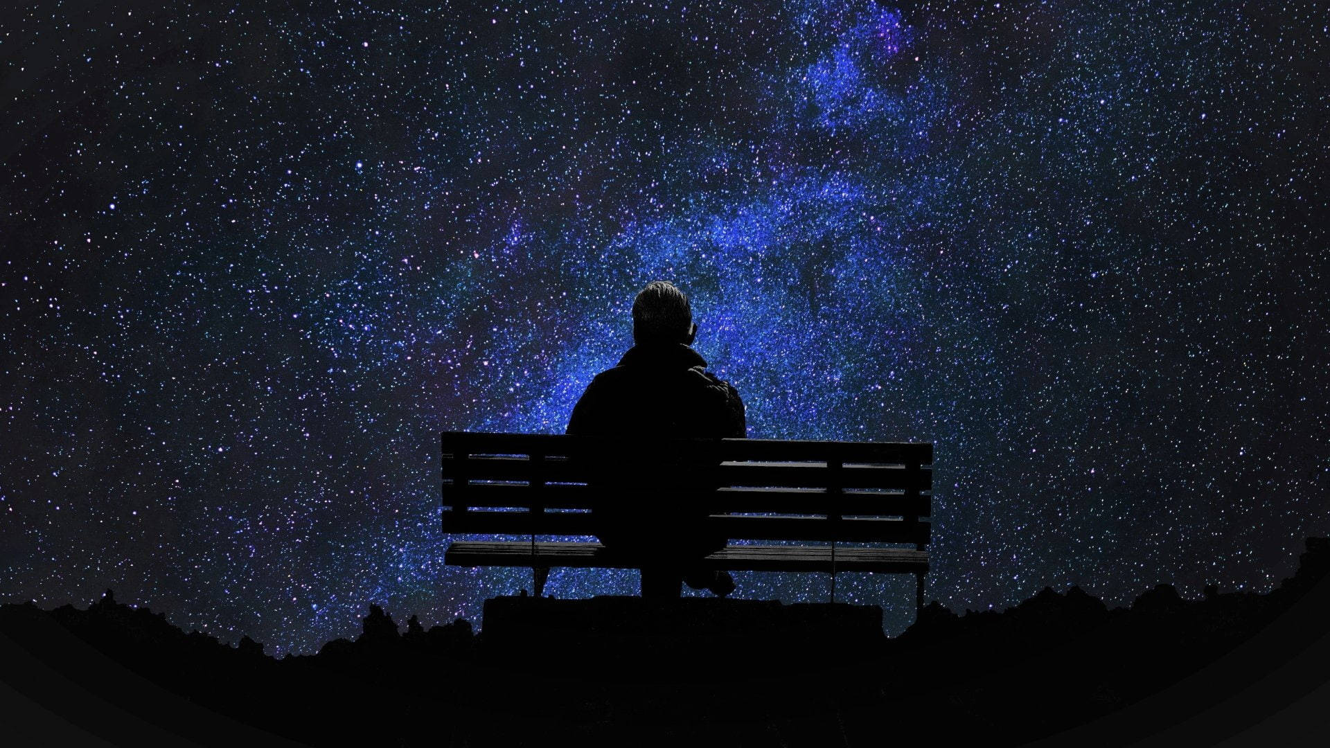 Alone 桌布 壁紙 — 一個孤獨的身影坐在長椅上，以剪影仰望充滿鮮豔藍色星雲的壯麗星空。