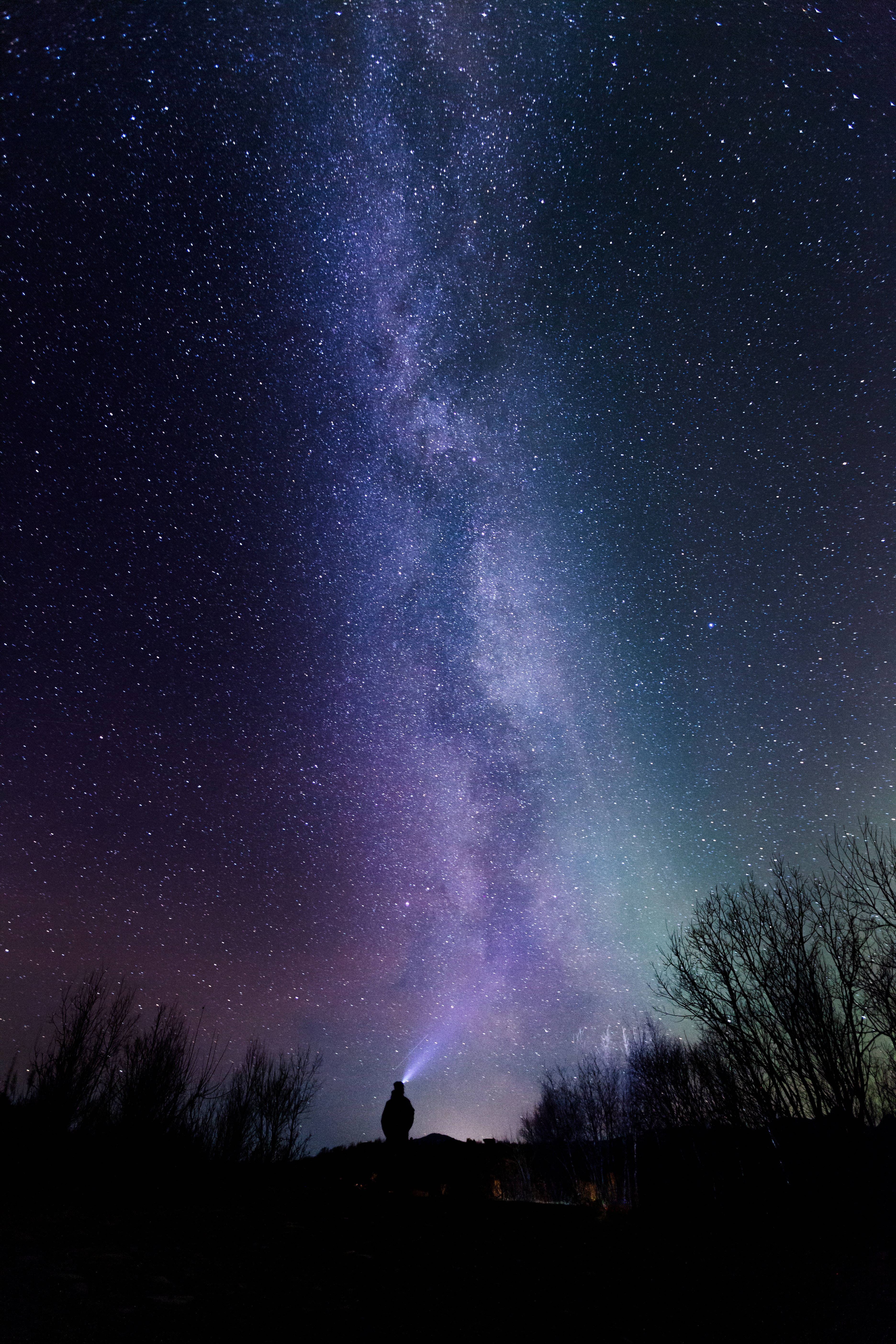 Stars 桌布 壁紙 — 一個孤獨的身影夜晚站在山丘上，仰望橫跨滿天星空的鮮豔紫色和藍色銀河系。