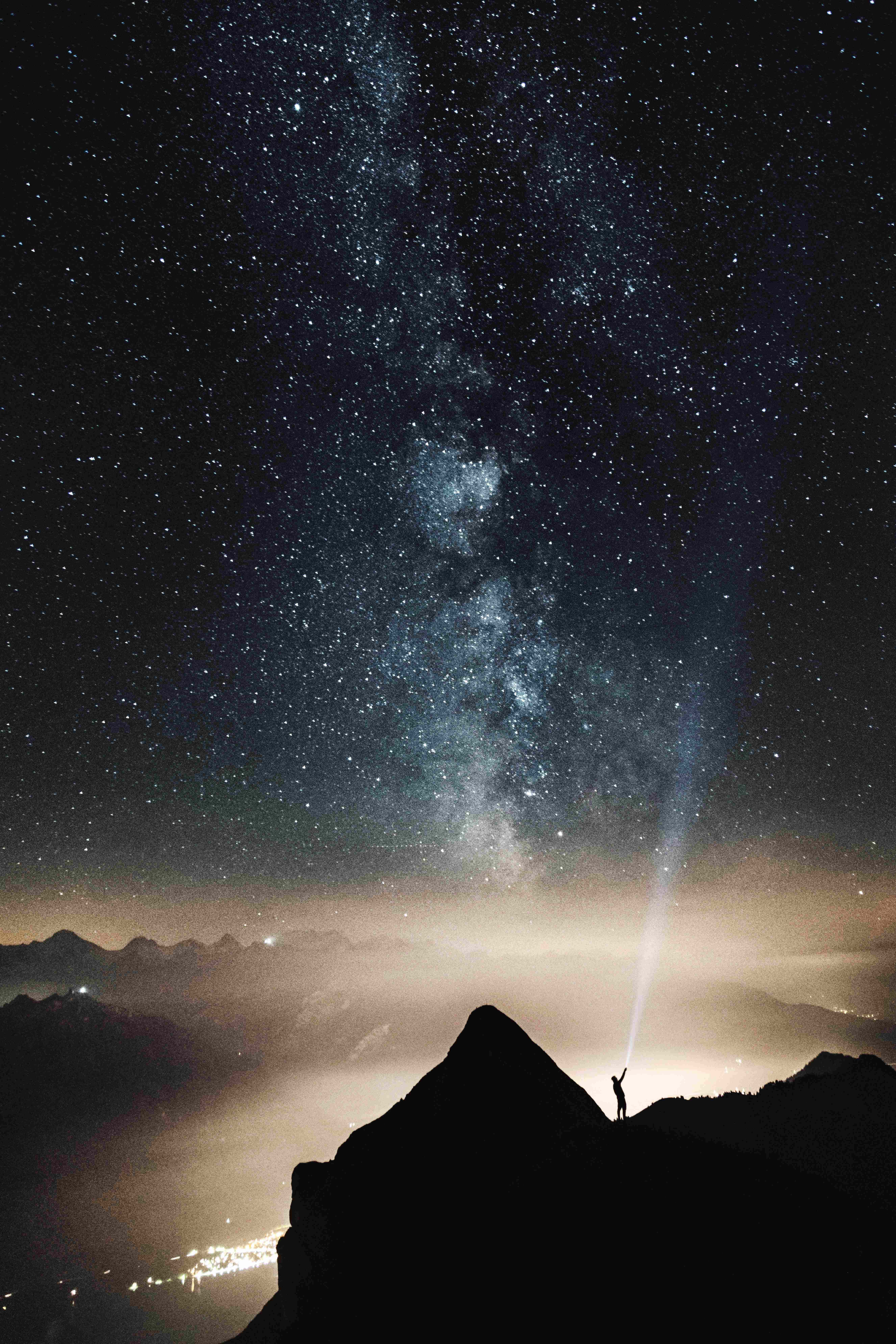 iPhone 桌布 壁紙 — 一個孤獨的身影夜晚站在山頂，將手電筒向上照向銀河系。