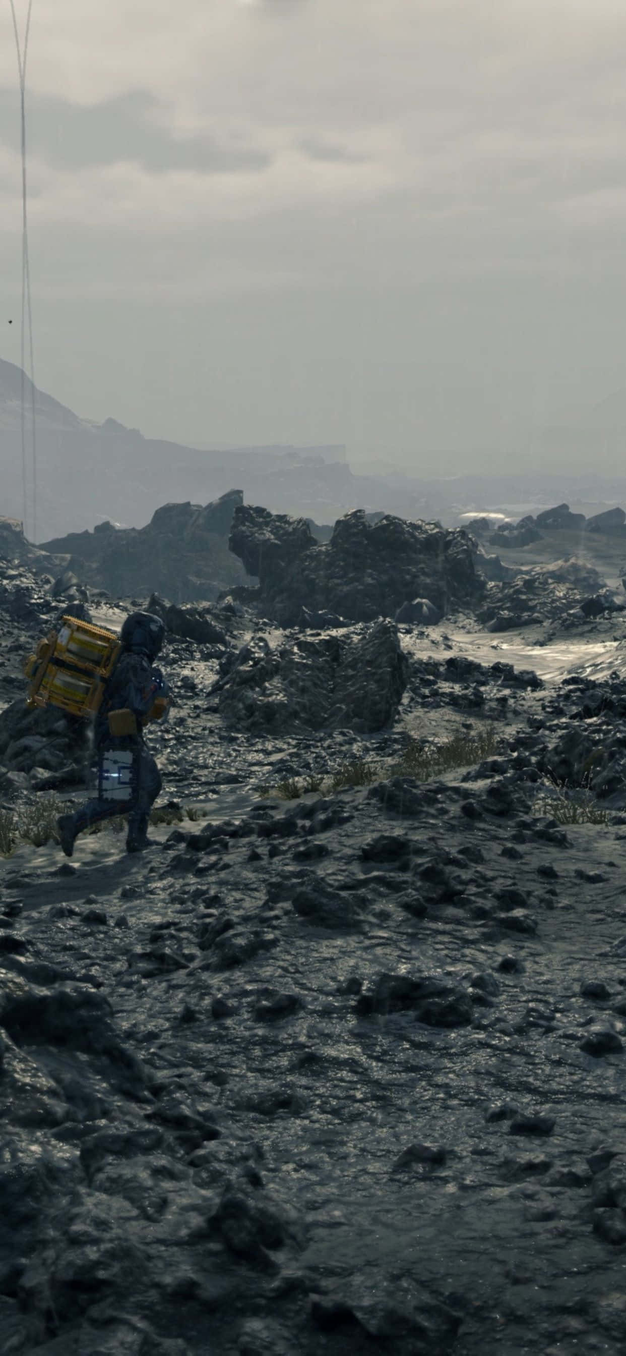 iPhone Xs Max Death Stranding 桌布 壁紙 — 一個孤獨的身影戴著頭盔和背包，在朦朧的天空下穿越荒涼的岩石地形。