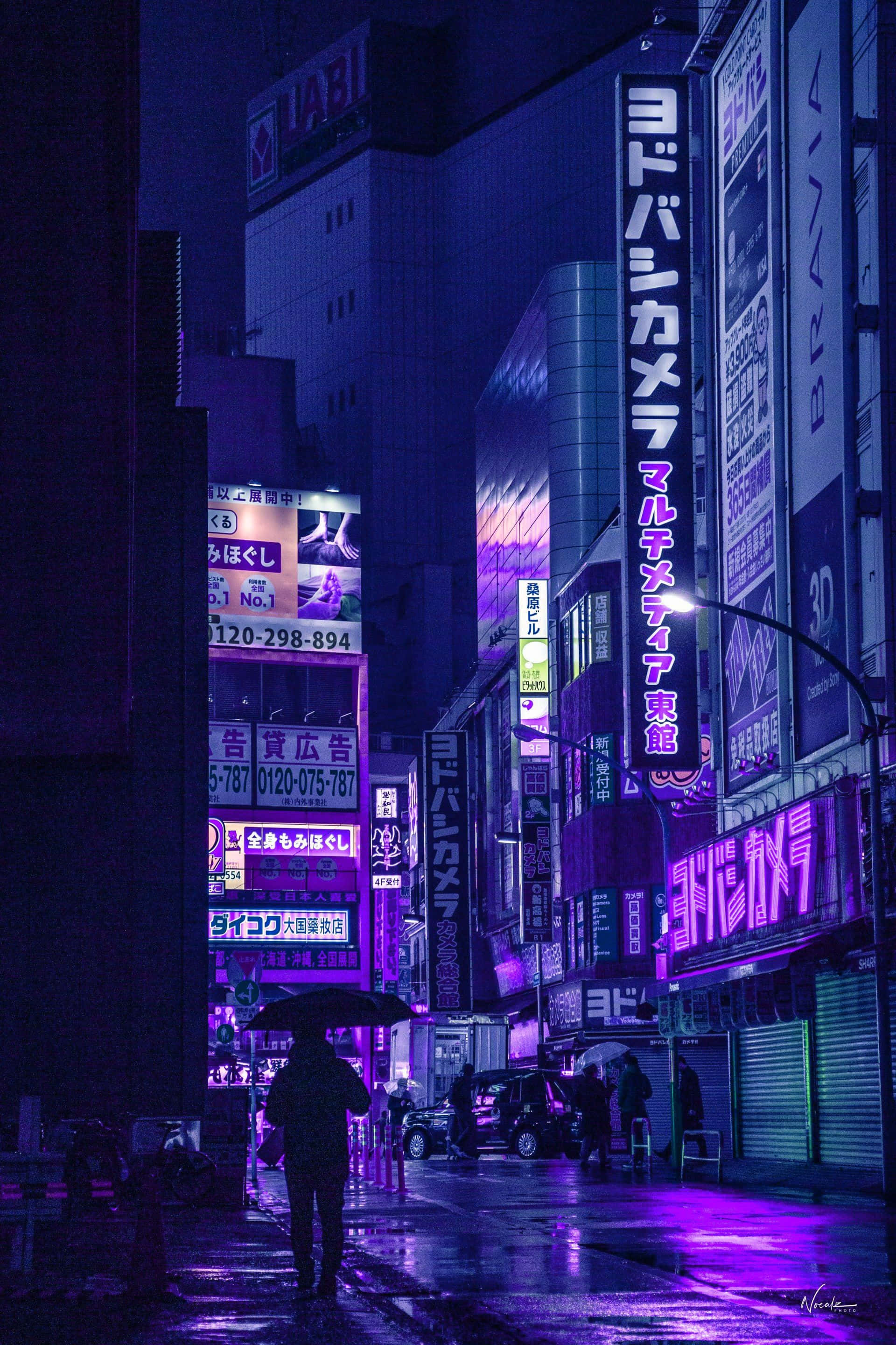桌布 壁紙 — 一個孤獨的身影撐著傘，在雨濕的東京霓虹街頭夜行，發光的招牌倒映在濕漉漉的路面上。