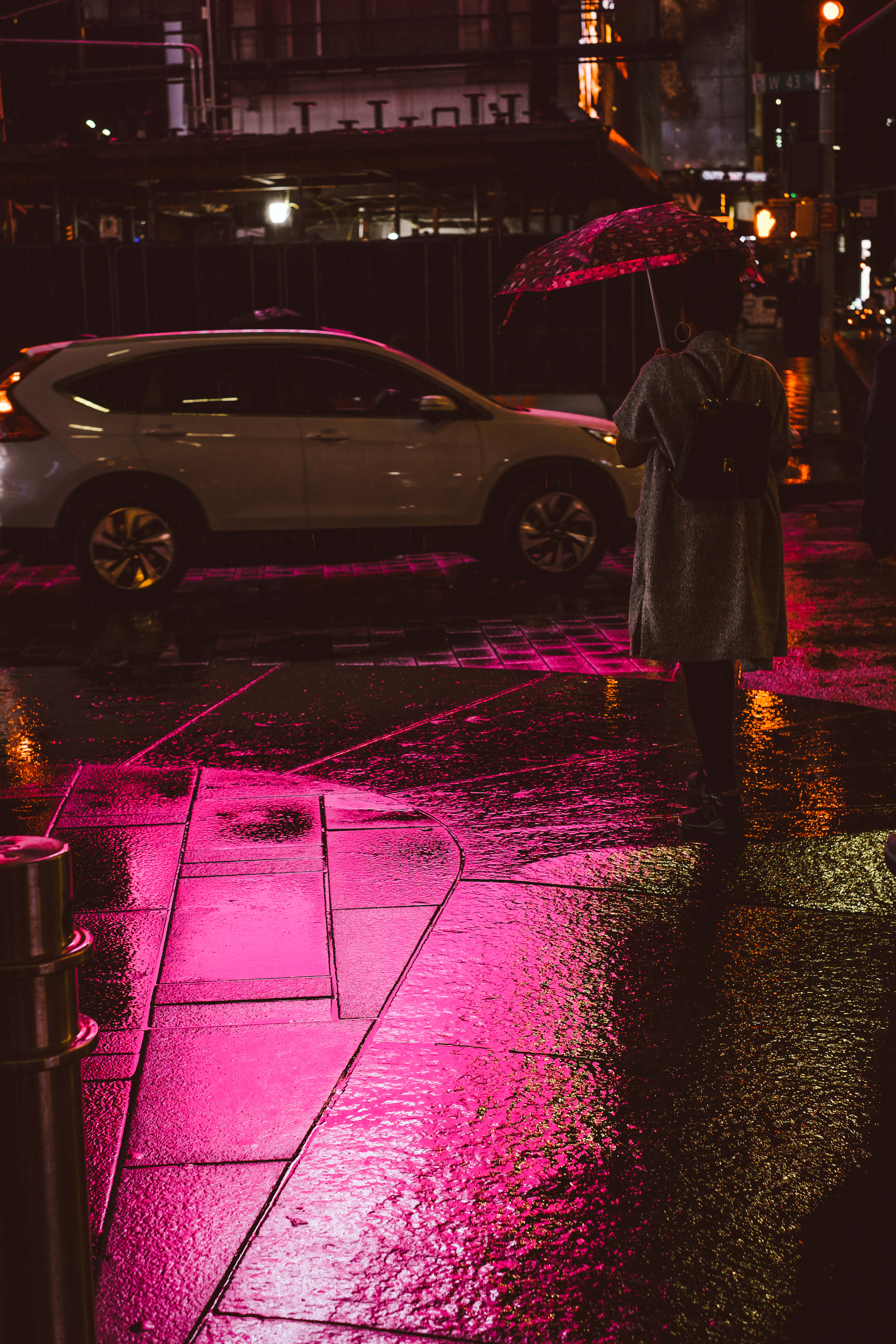憂鬱美學 桌布 壁紙 — 一個孤獨的身影撐著傘，走在被雨水浸濕的城市街道上，沐浴在鮮豔的粉紅色霓虹燈反射中。
