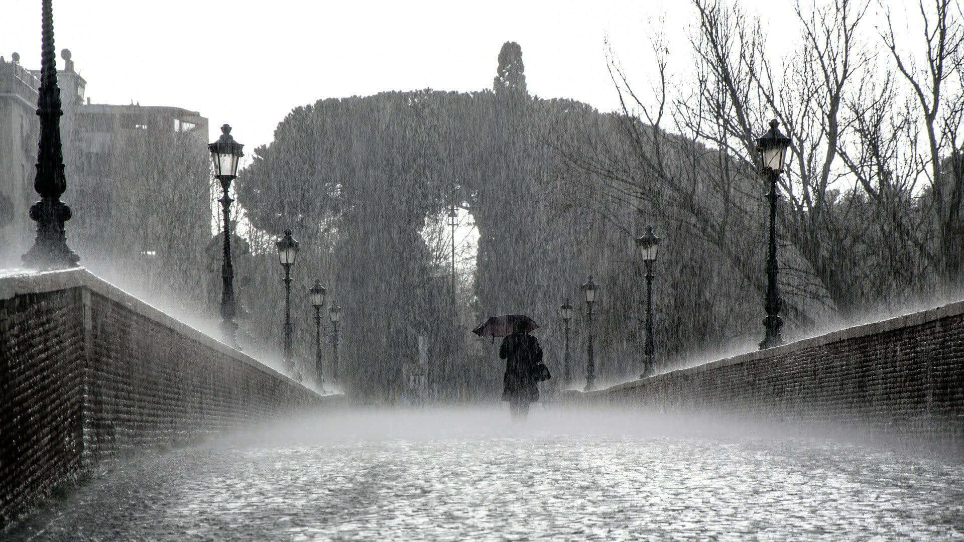 下雨 桌布 壁紙 — 一個孤獨的身影撐著雨傘，在佈滿復古路燈的石橋上冒著大雨行走。