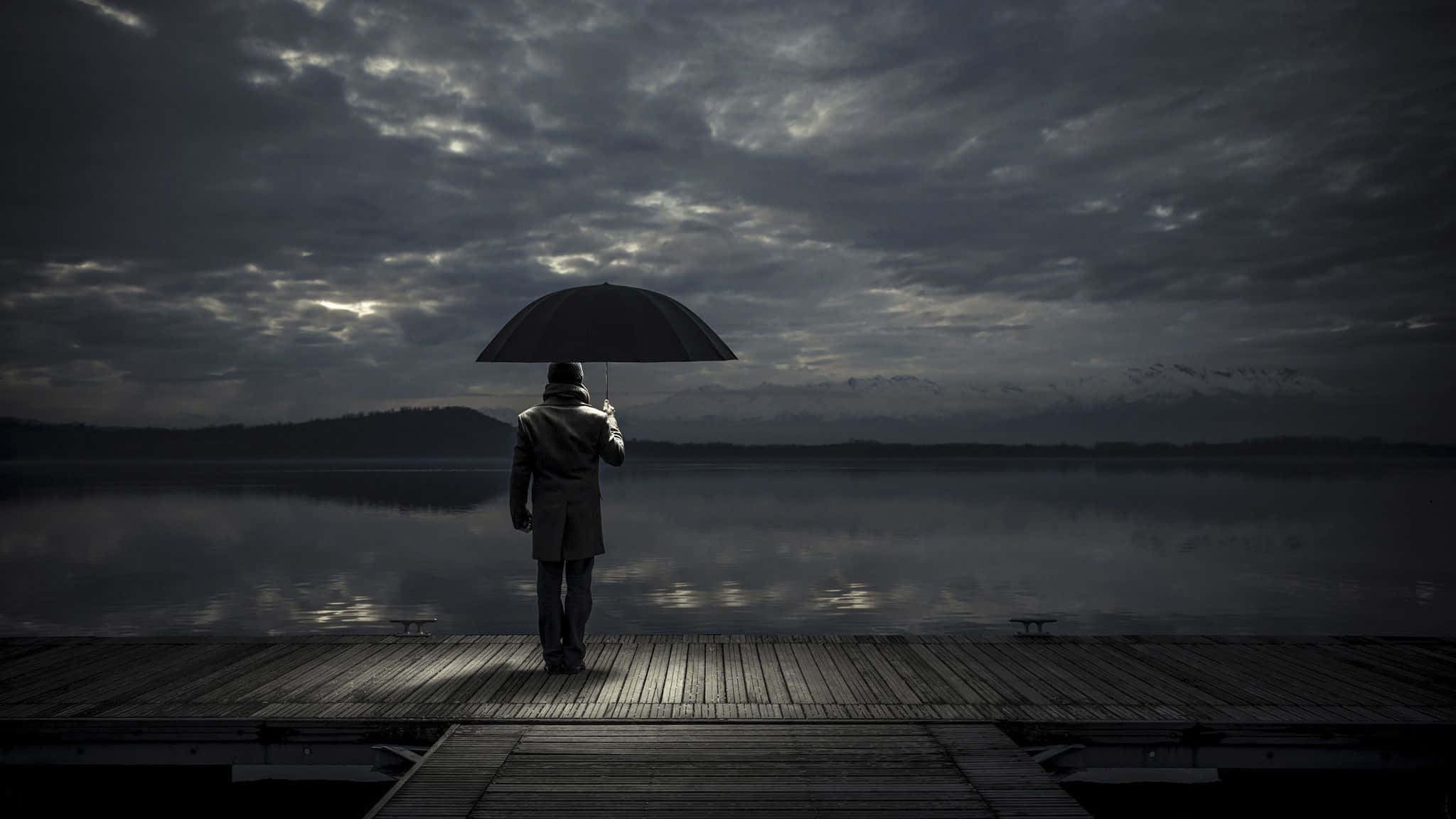 Lonely 桌布 壁紙 — 一個孤獨的身影撐著雨傘，站在木製碼頭上，凝視著暴風雨灰色天空下霧氣瀰漫的湖泊。