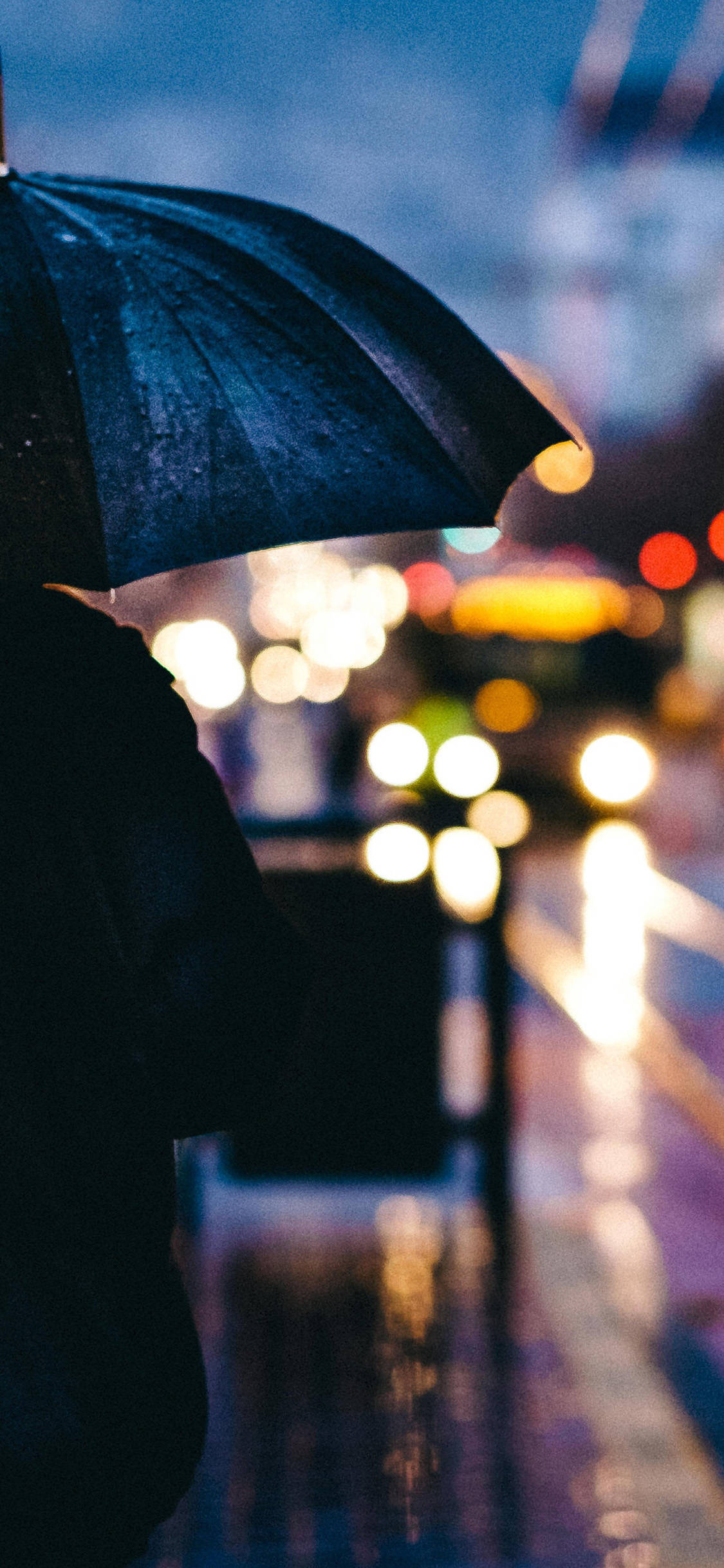 iPhone 桌布 壁紙 — 一個孤獨的身影撐著黑色雨傘擋雨，模糊的城市燈光在潮濕的夜晚溫暖地閃爍。