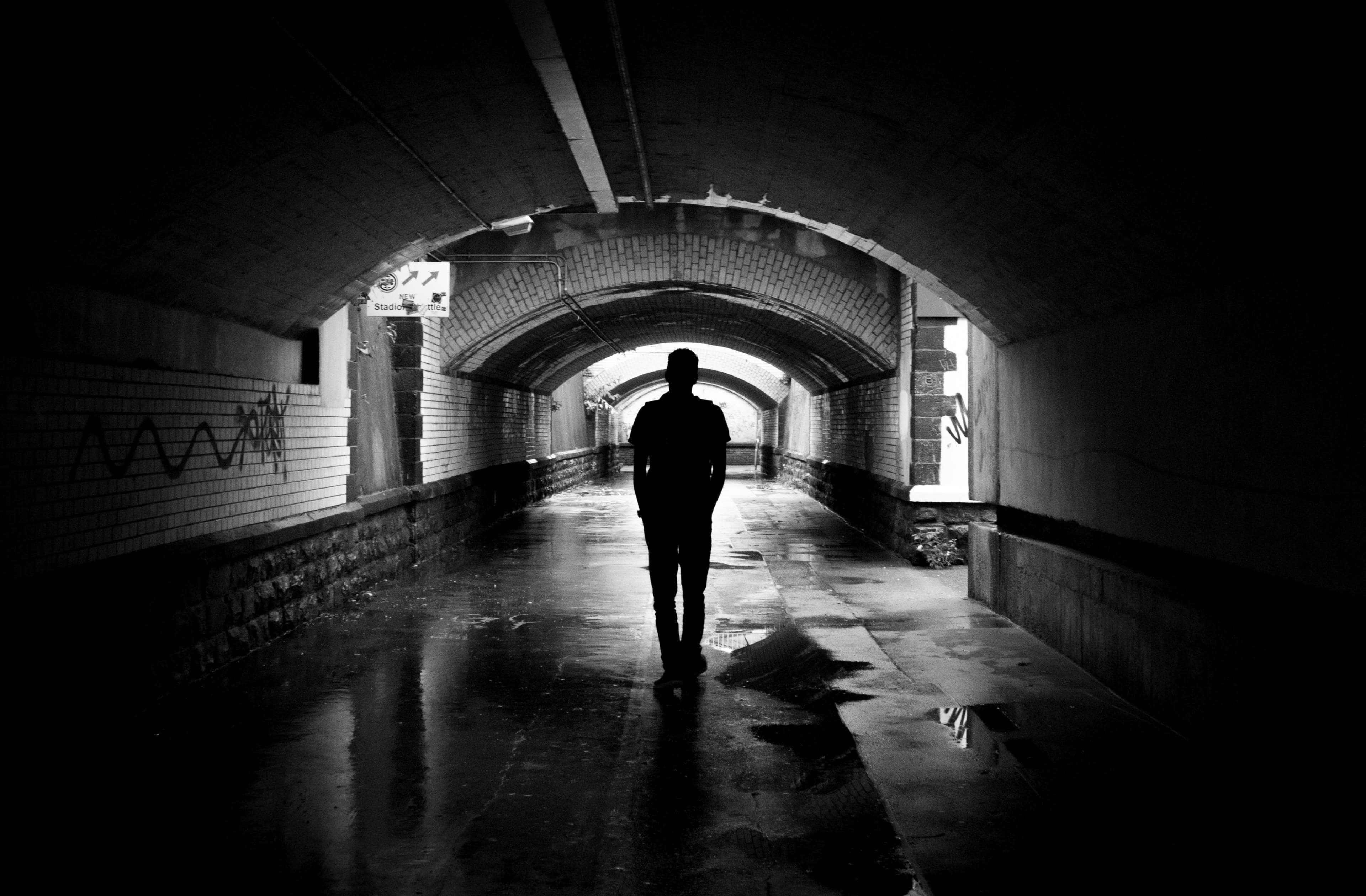 Dark Underground 桌布 壁紙 — 一個孤獨的身影沿著潮濕、佈滿塗鴉的磚砌隧道走向遠方的光線。