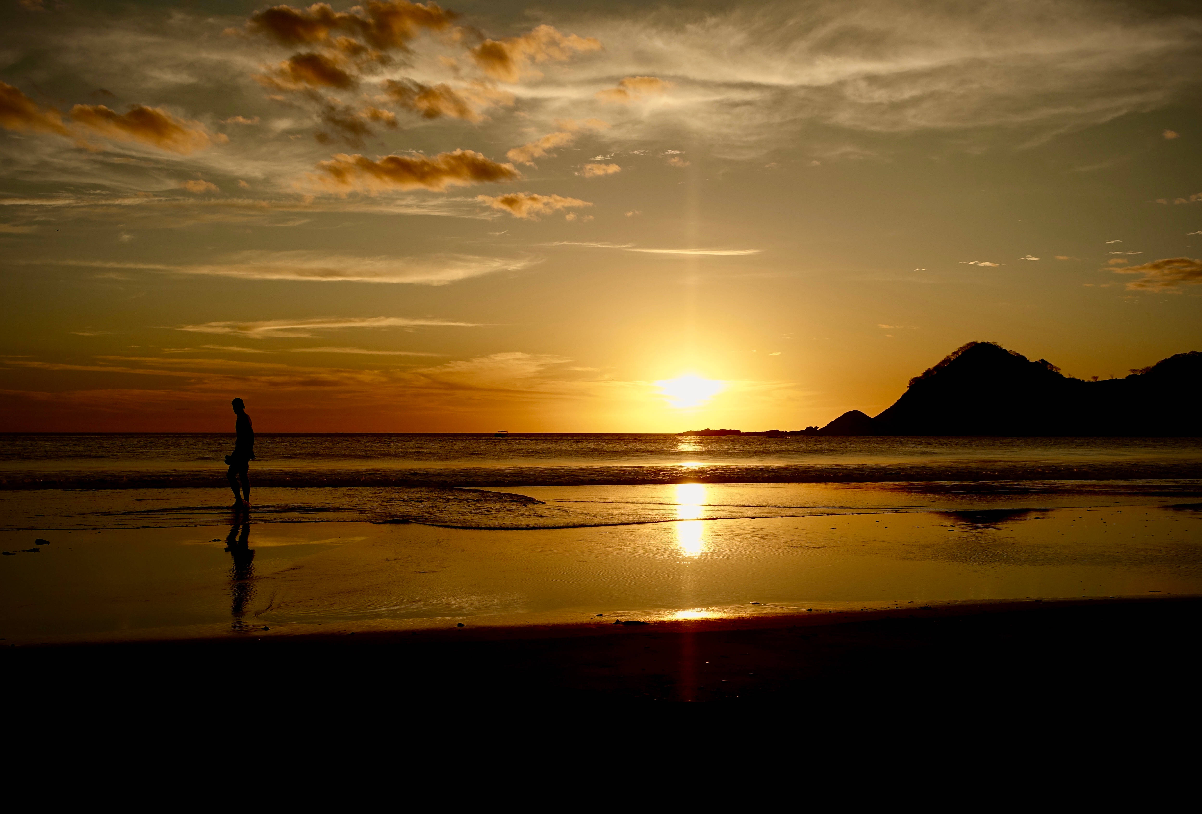 Nicaragua 桌布 壁紙 — 一個孤獨的身影沿著濕漉漉的海灘行走，夕陽在遠山後落下，將金色光芒灑在水面上。