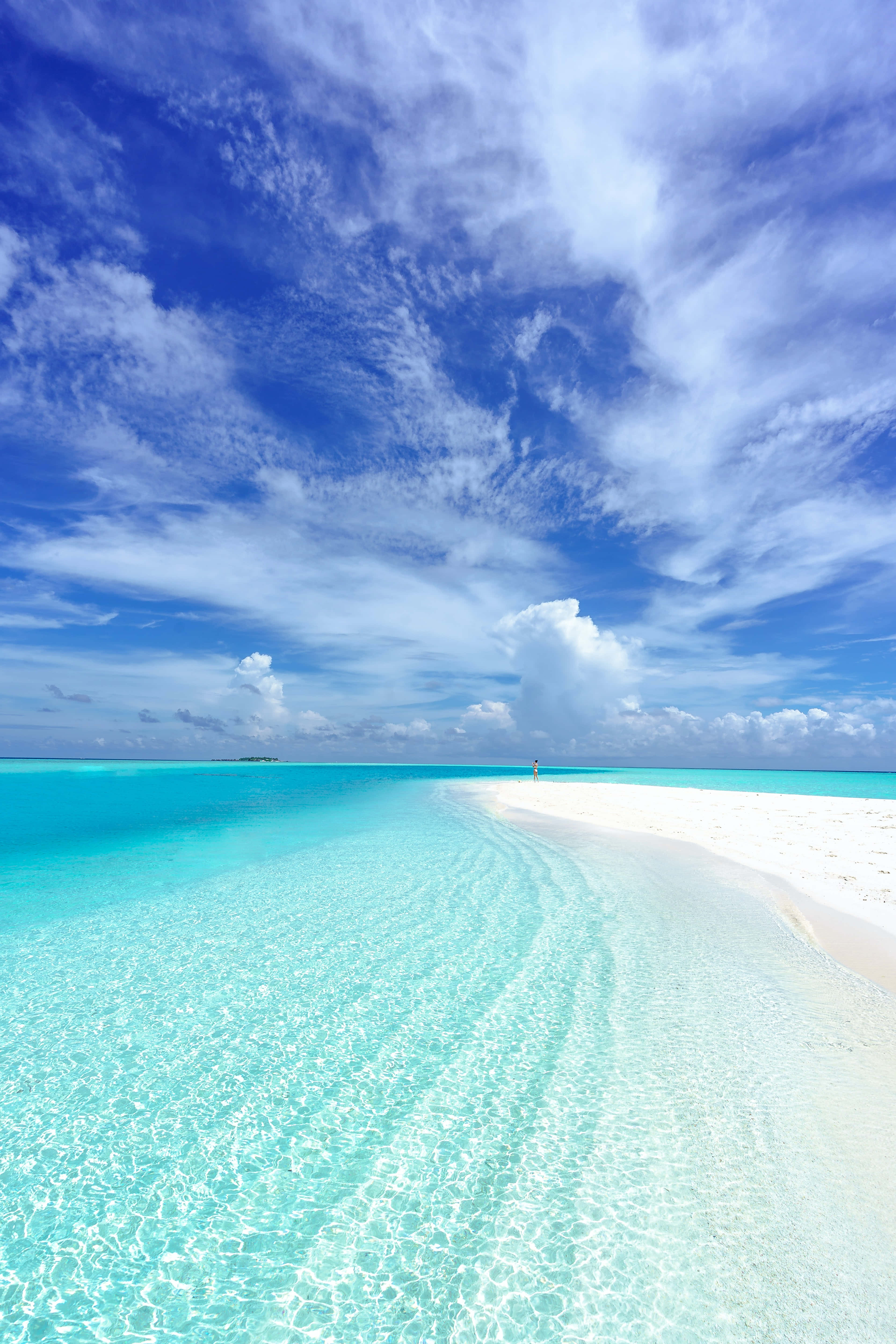 Beautiful Beach 桌布 壁紙 — 一個孤獨的身影沿著純淨的白色沙洲，在清澈碧綠的海水中行走，頭頂是廣闊的藍天，點綴著縷縷薄雲。