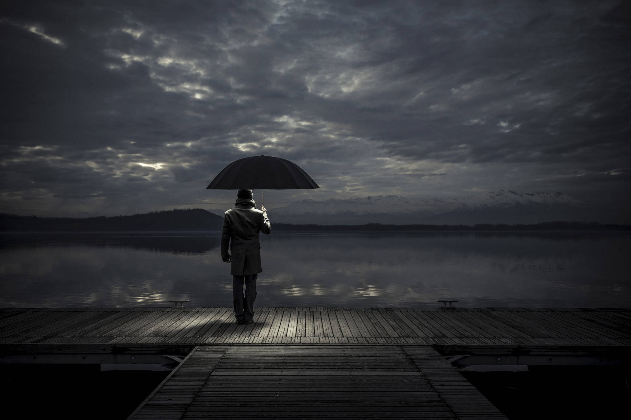 melancholy 桌布 壁紙 — 一個孤獨的身影穿著外套，在木製碼頭上撐著雨傘，陰沉多雲的天空倒映在平靜的水面上。