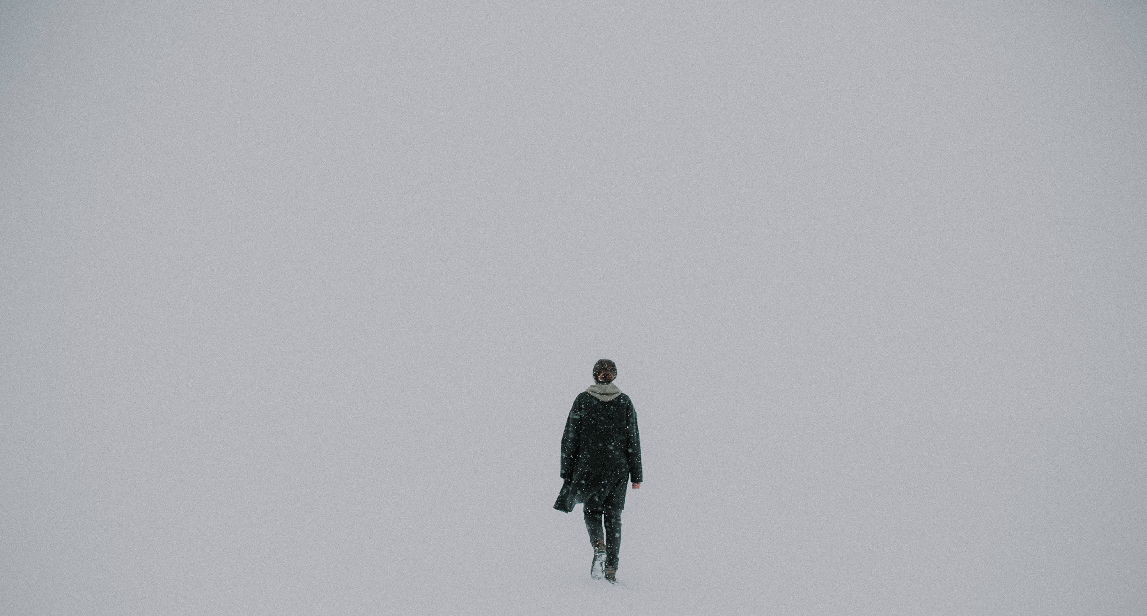Forever Alone 桌布 壁紙 — 一個孤獨的身影穿著深色外套，在陰天之下走過廣闊的雪地。