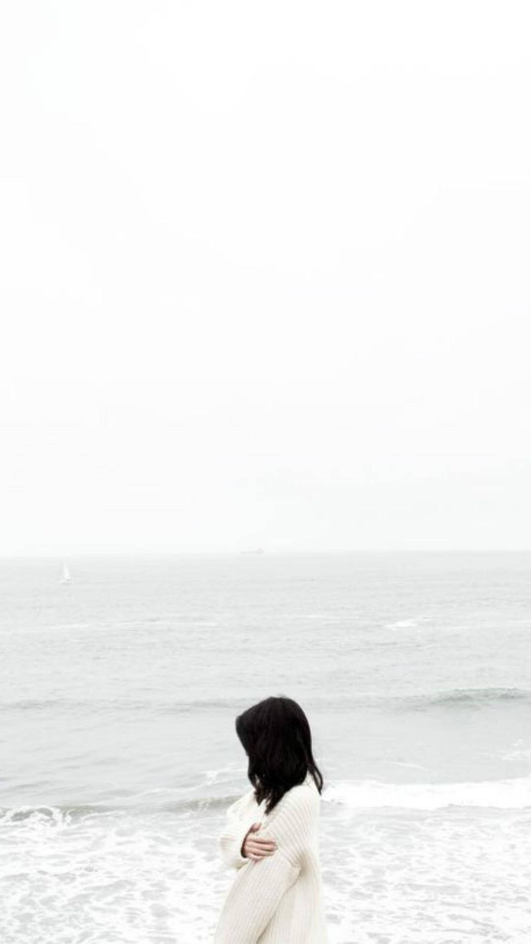 Alone 桌布 壁紙 — 一個孤獨的身影穿著白色針織毛衣，在灰濛濛的日子裡站在霧濛濛的海岸邊擁抱自己。
