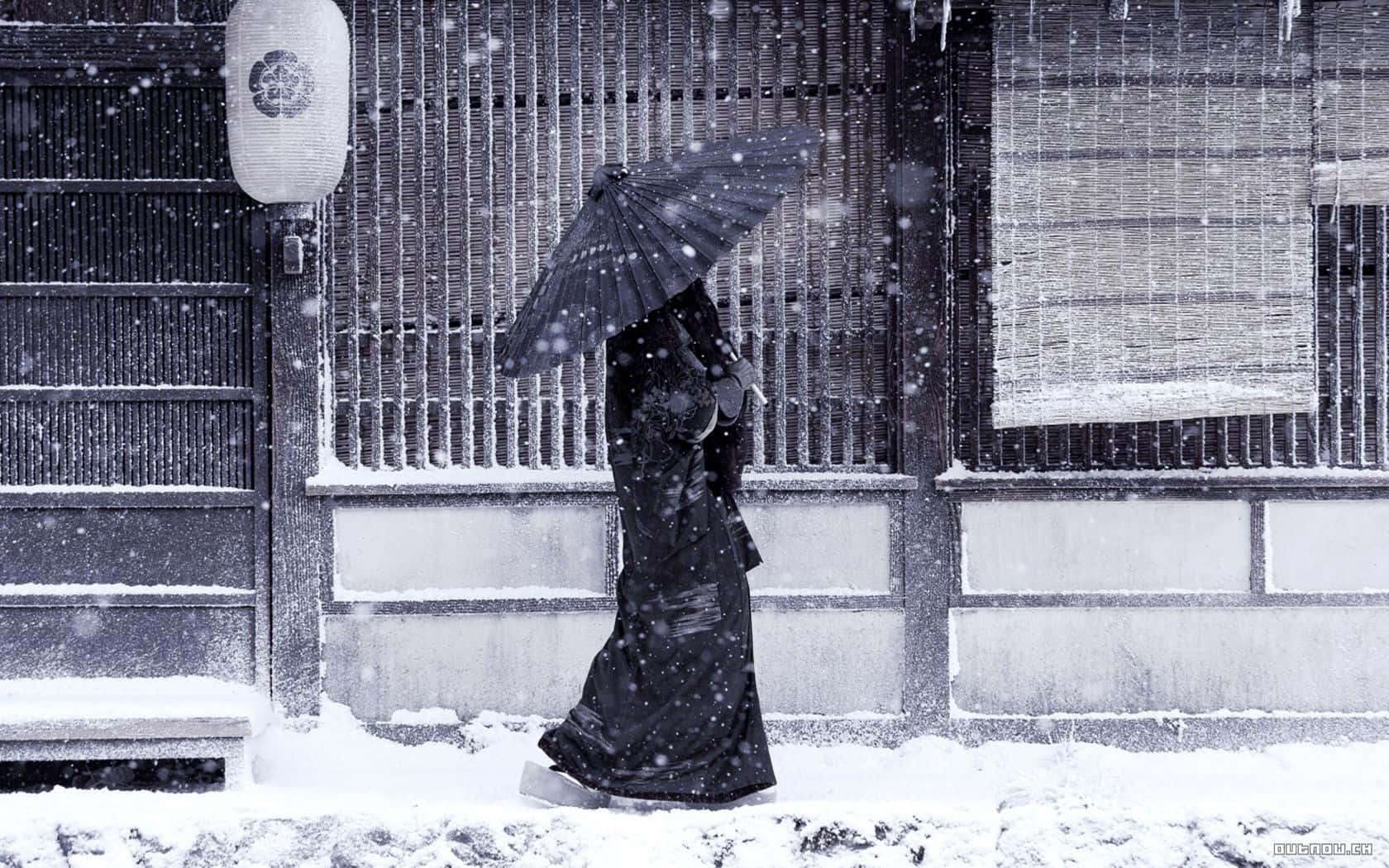 High Resolution Snow 桌布 壁紙 — 一個孤獨的身影穿著黑色和服，在飄雪中走過一棟傳統日式建築，旁邊有竹簾和紙燈籠。