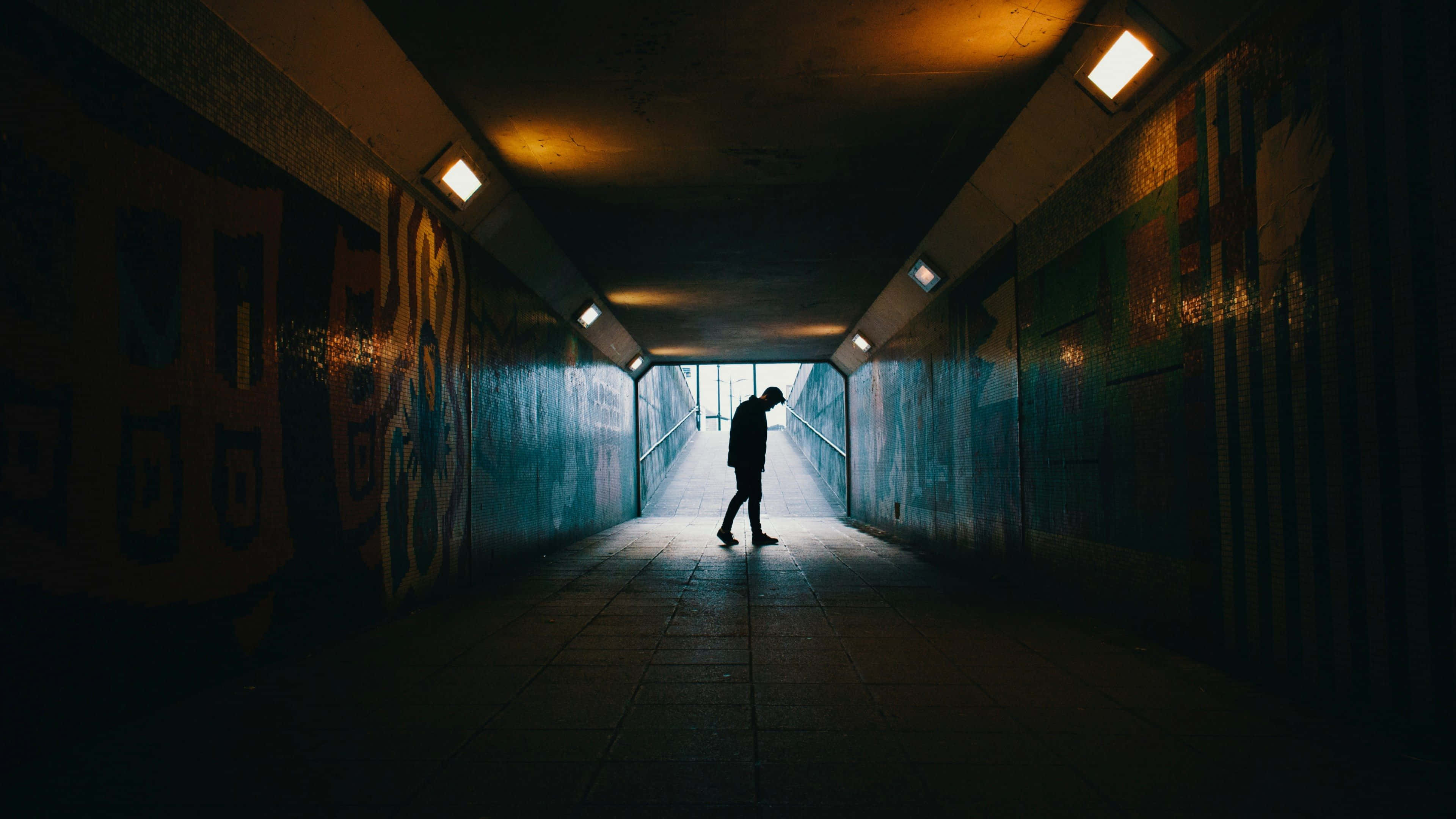 Subway 桌布 壁紙 — 一個孤獨的身影穿過一條燈光昏暗的城市隧道，牆上有塗鴉，頭頂有溫暖的燈光。