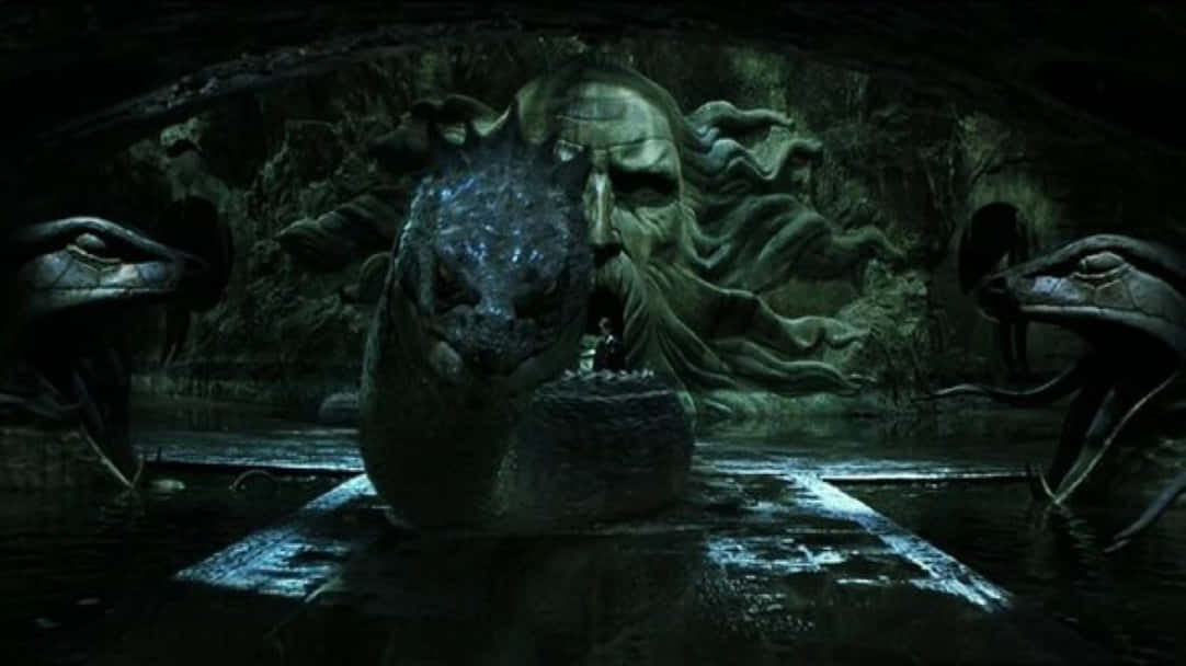 Harry Potter Serpent 桌布 壁紙 — 一個孤獨的身影站在一個巨大、怪誕、帶有蛇形特徵的石頭頭顱前，身處一個黑暗潮濕的洞穴中。