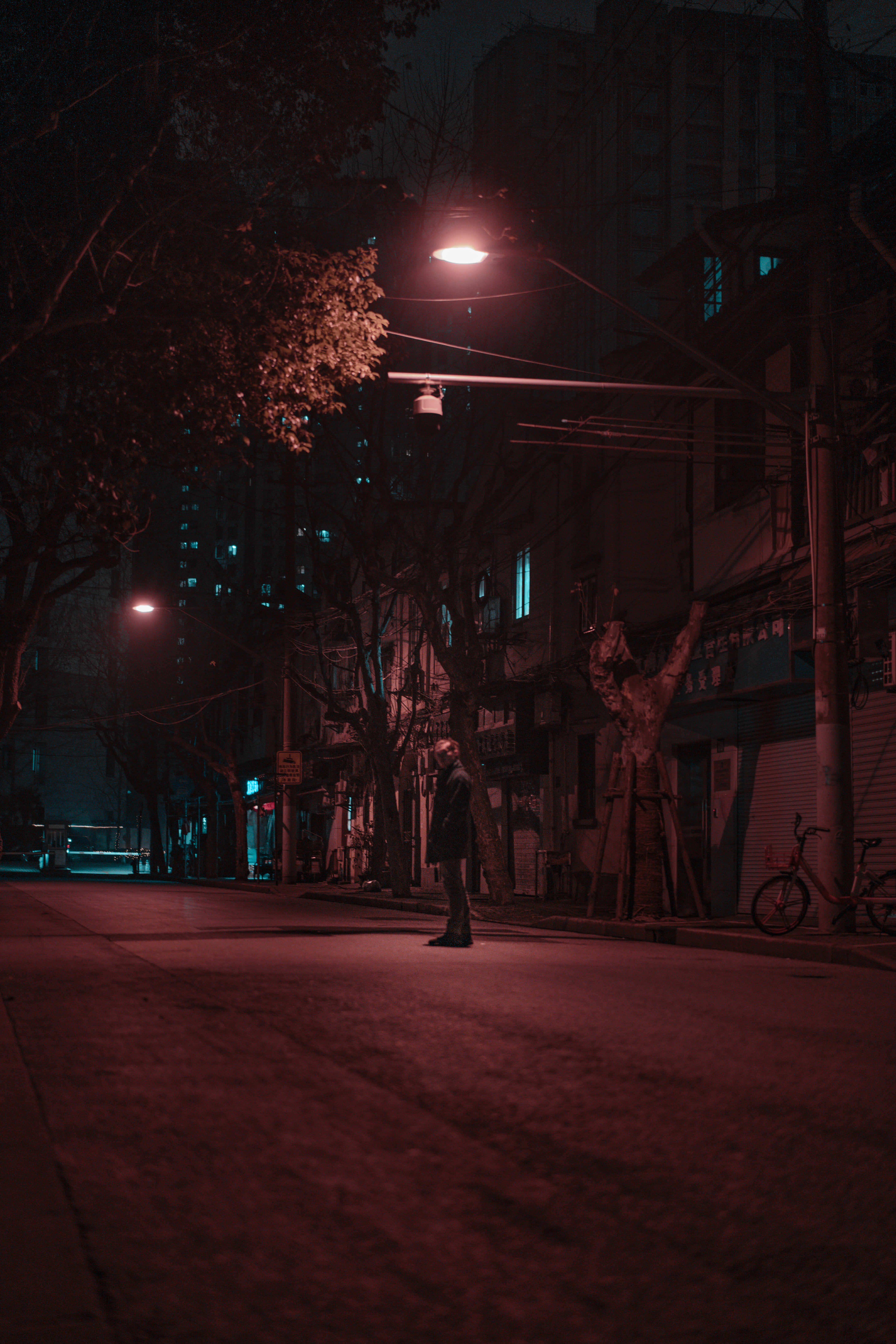 Sad Vibes 桌布 壁紙 — 一個孤獨的身影站在一條寧靜的城市街道上，被深紅色的暮色籠罩，在一盞發光的街燈下。