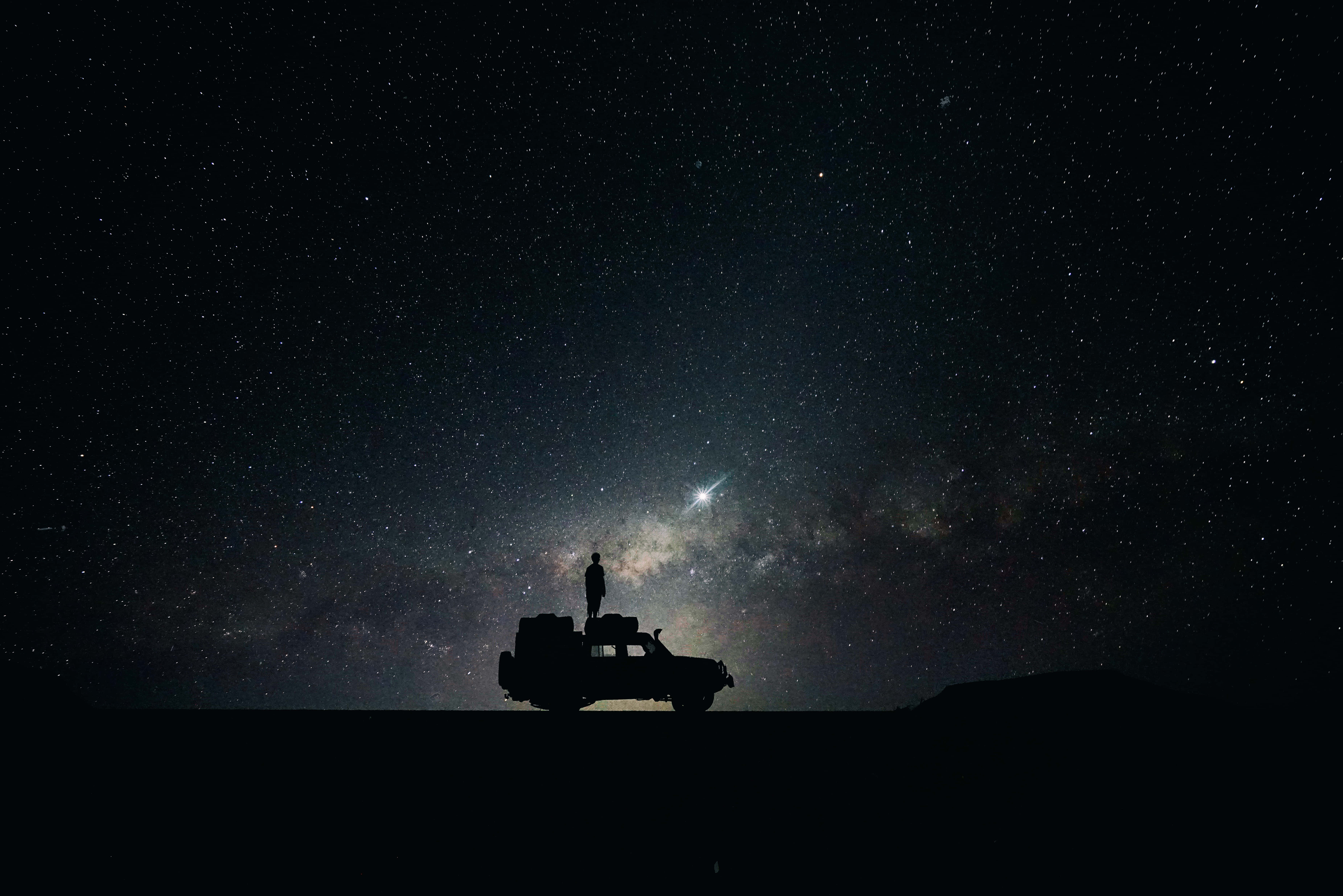 Alone 桌布 壁紙 — 一個孤獨的身影站在一輛停泊的SUV上，頭頂是令人嘆為觀止的星空，銀河在閃耀。