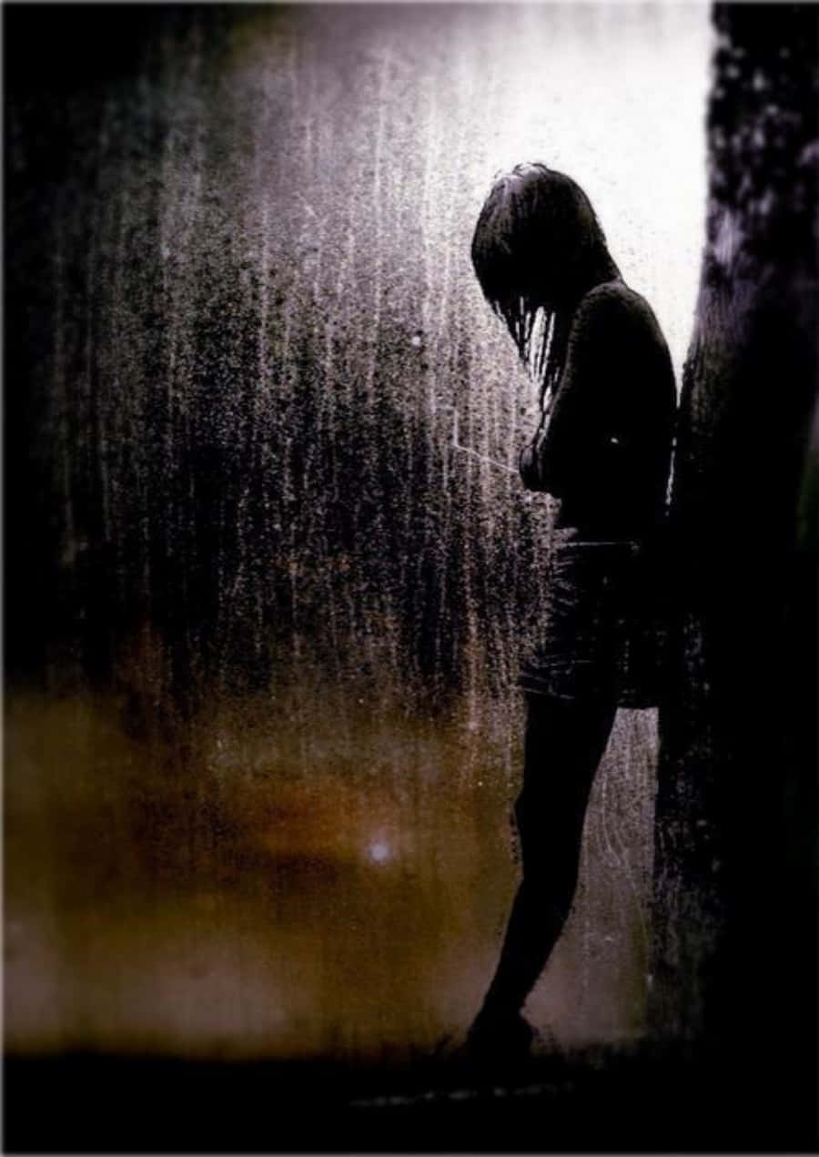 Alone 桌布 壁紙 — 一個孤獨的身影站在傾盆大雨中，靠著牆壁，在強烈的背光下低頭沉默。